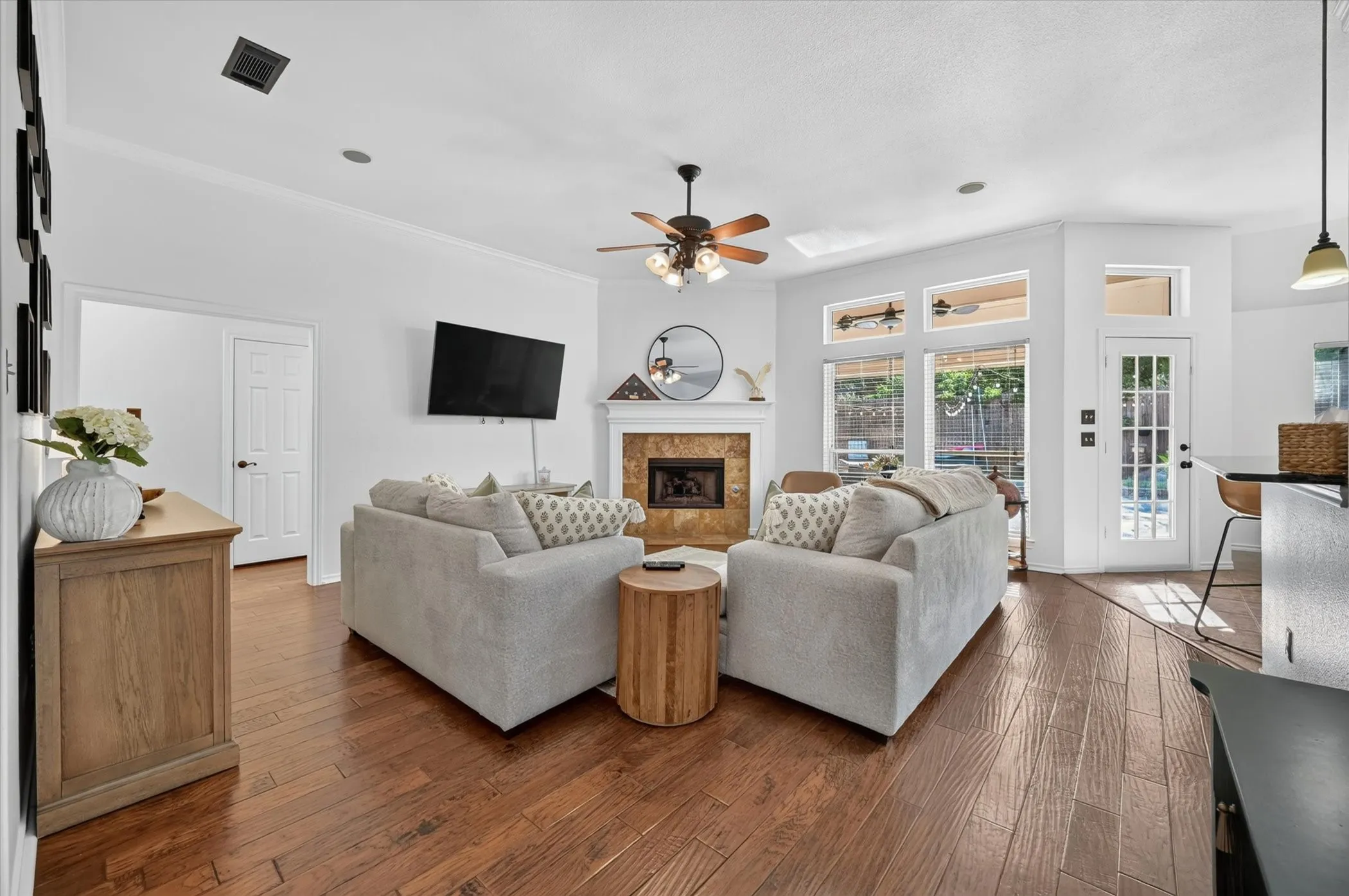 Living area featuring wood-finish flooring, a fireplace with a stone surround and mantel, and a ceiling fan
