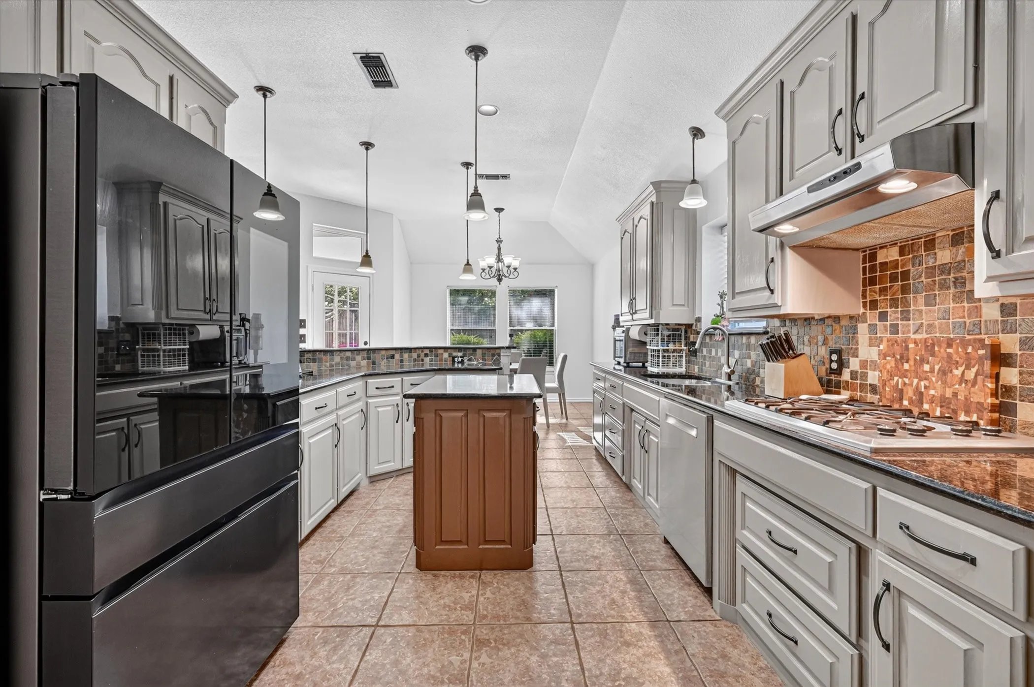 Spacious kitchen featuring gray cabinetry, dark countertops, a tiled backsplash, and a central island with a wood-finish base