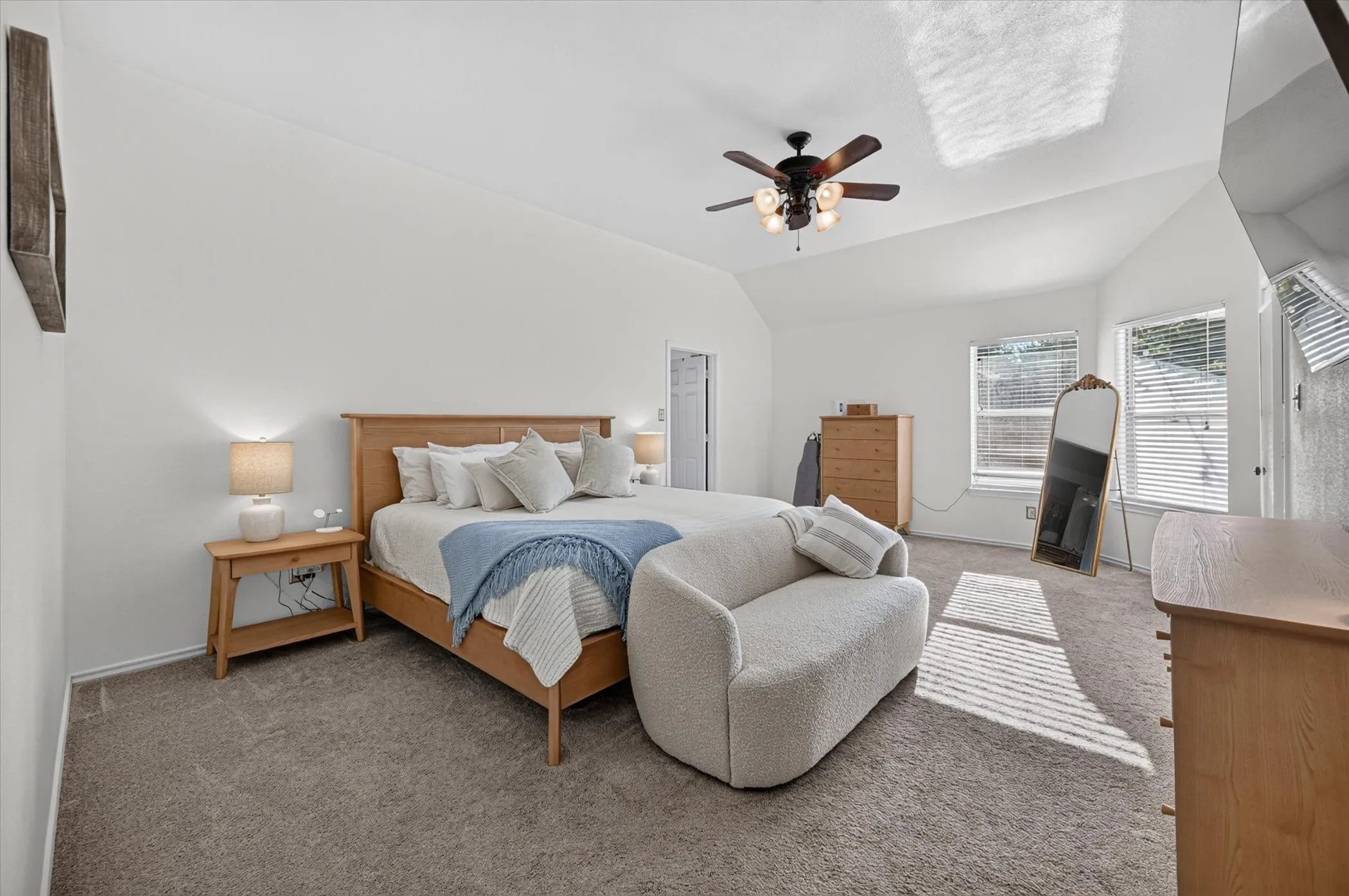 Spacious room featuring vaulted ceilings, neutral carpeting, a ceiling fan with integrated lighting, and multiple windows with horizontal blinds