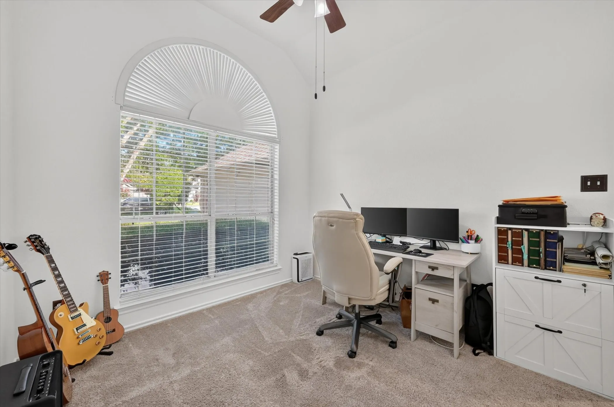 Vaulted ceiling room featuring an arched window with blinds, carpet flooring, and a ceiling fan