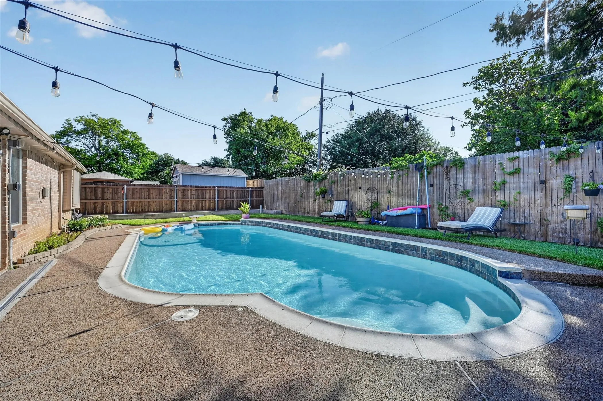 Resort-style backyard featuring a sparkling in-ground pool, expansive aggregate concrete patio, and string lighting