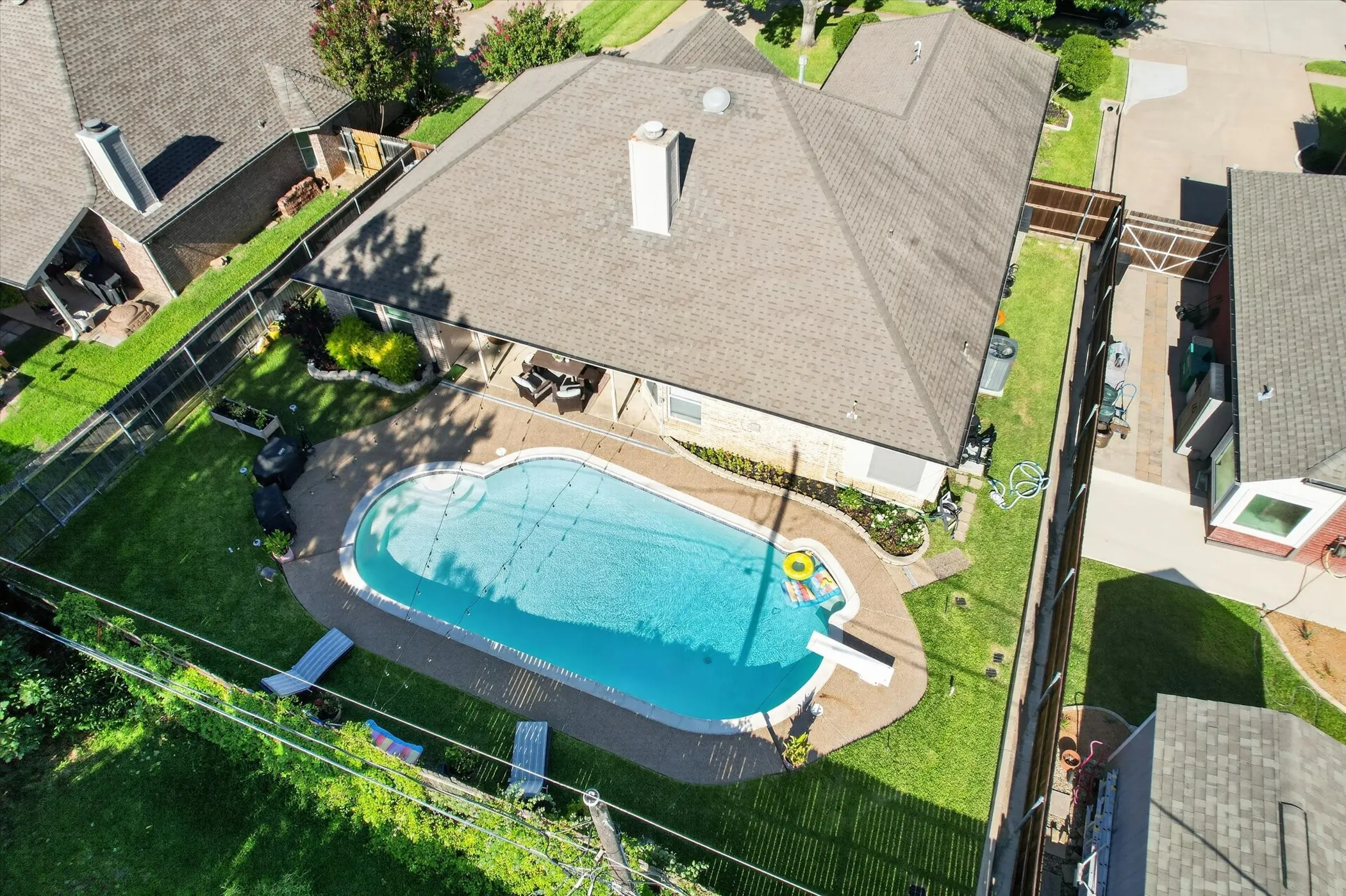 Backyard featuring a freeform swimming pool with a diving board, surrounding concrete patio, and a manicured lawn