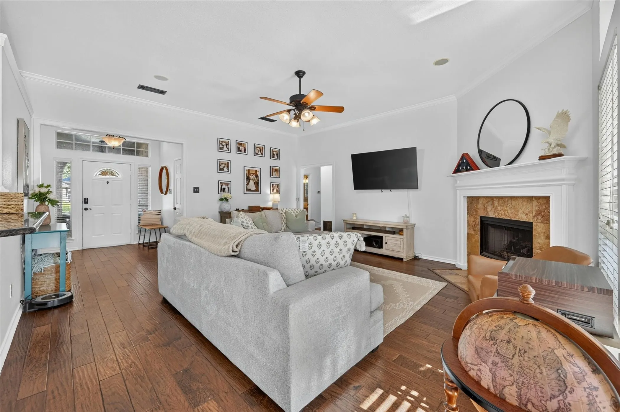 Spacious living area featuring wood-finish flooring, a ceiling fan, and a fireplace with a stone surround and white mantel
