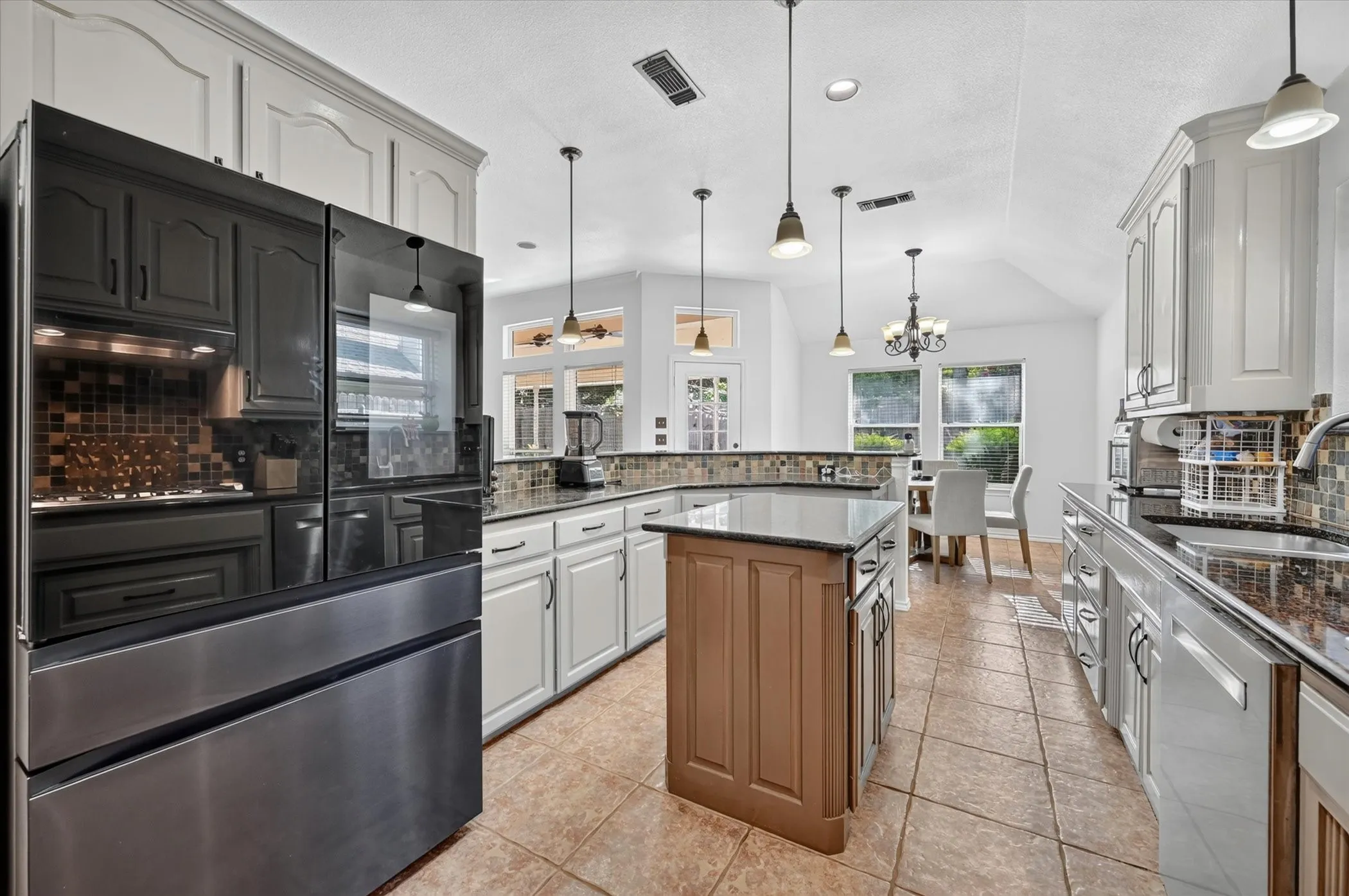 Kitchen featuring white cabinetry, dark stone countertops, a mosaic tile backsplash, and an island with a wood-finish base