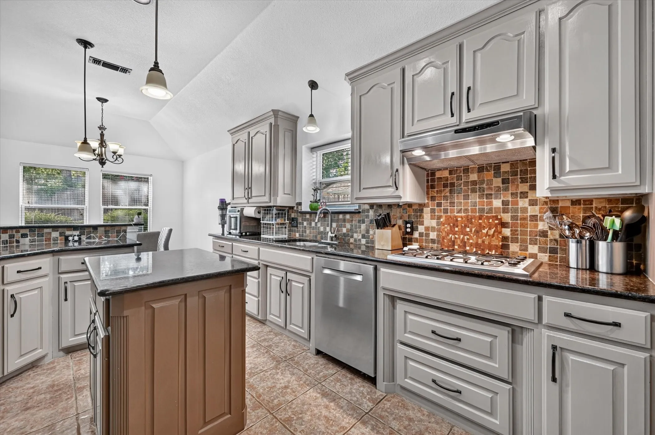Kitchen featuring light cabinetry with dark hardware, dark countertops, a tiled backsplash, and stainless steel appliances