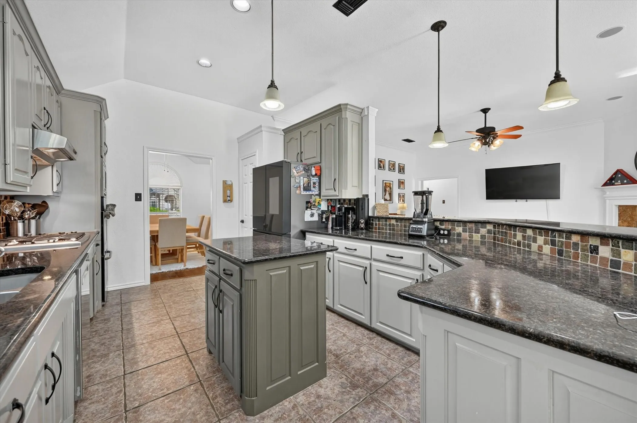 Kitchen featuring grey cabinetry, dark stone countertops, tile backsplash, tile flooring, and a central island