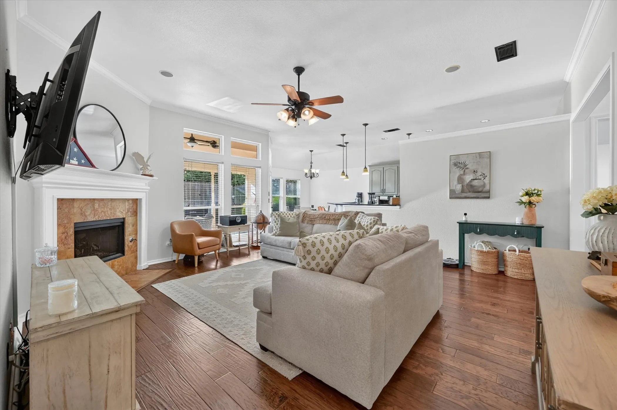 Spacious living area featuring wood-finish flooring, a tiled fireplace with a classic mantel, and crown molding
