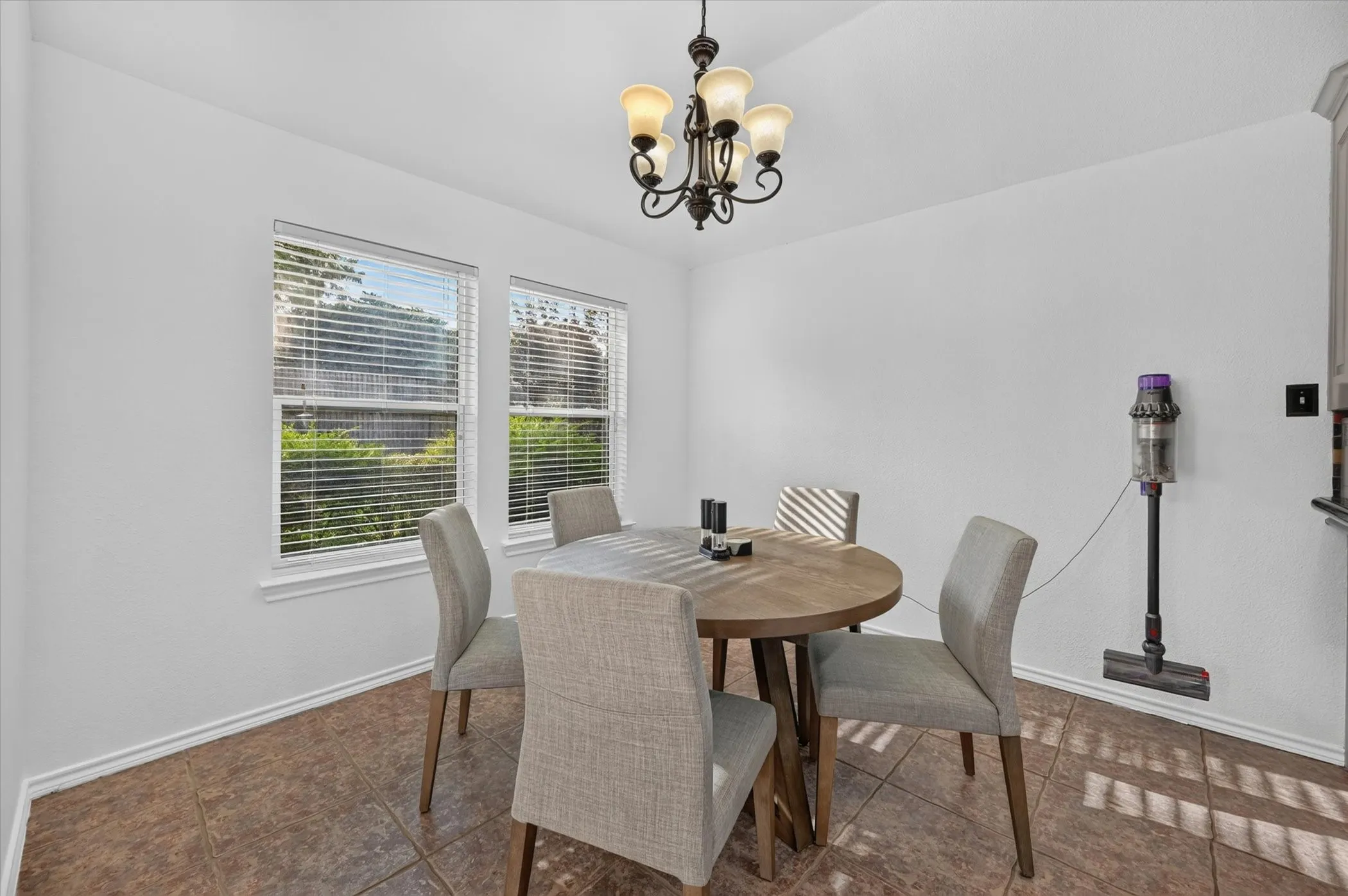 Dining area featuring tile flooring, two windows with blinds, and a multi-light chandelier