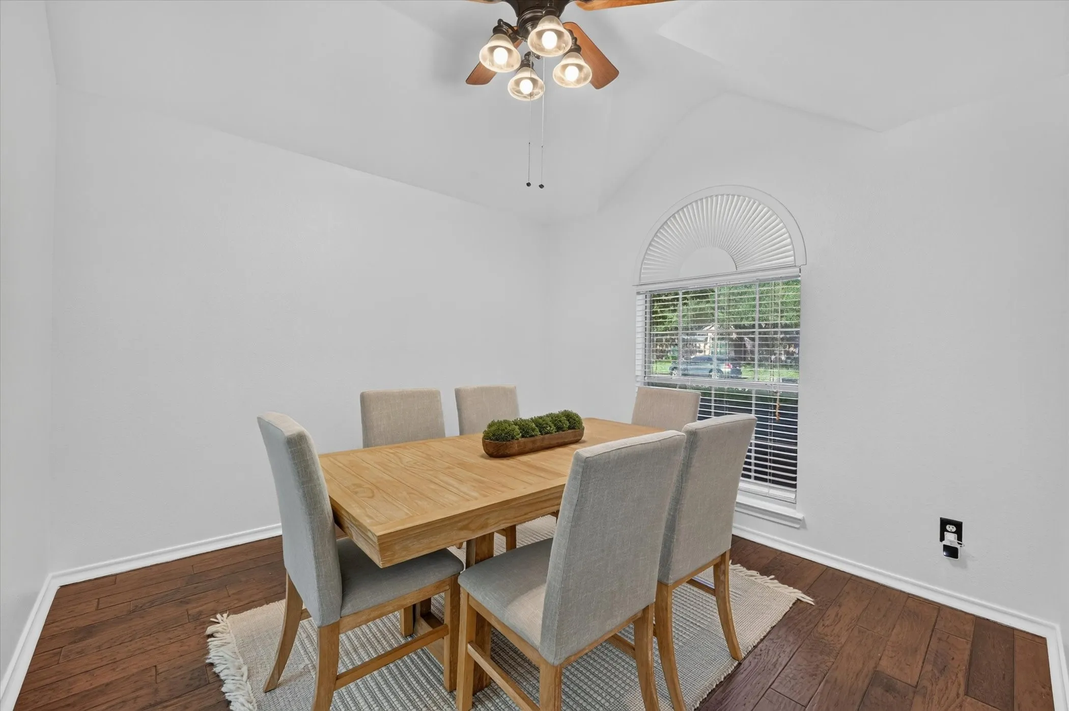 Vaulted ceiling featuring a ceiling fan with integrated lighting, wood-finish flooring, and an arched window with blinds
