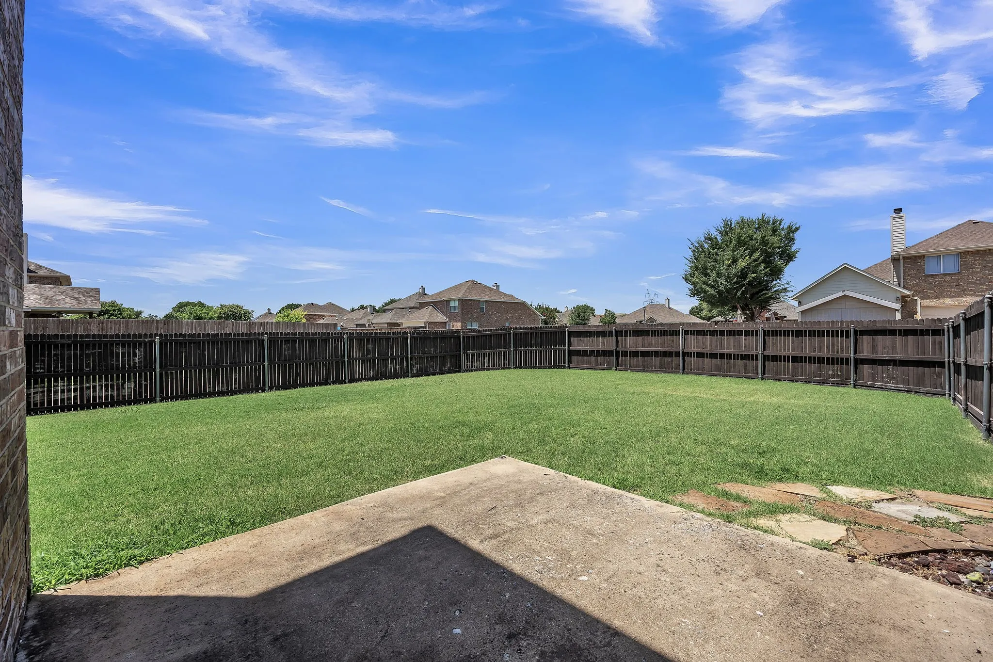 Expansive backyard featuring a manicured lawn, full perimeter fencing, and a concrete patio