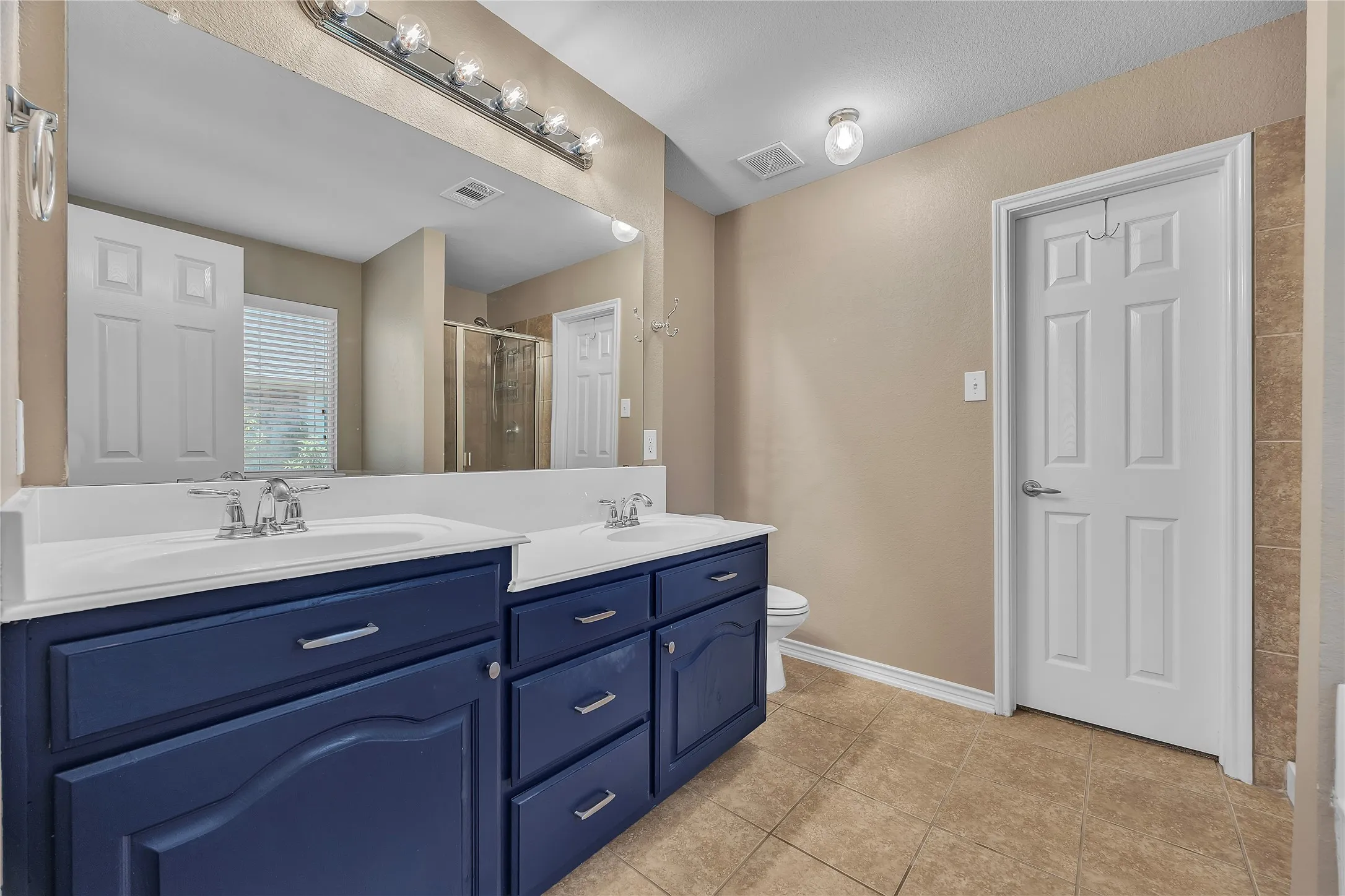 Dual vanity with integrated sinks, ample cabinet storage, a large wall-mounted mirror, overhead vanity lighting, and tile flooring
