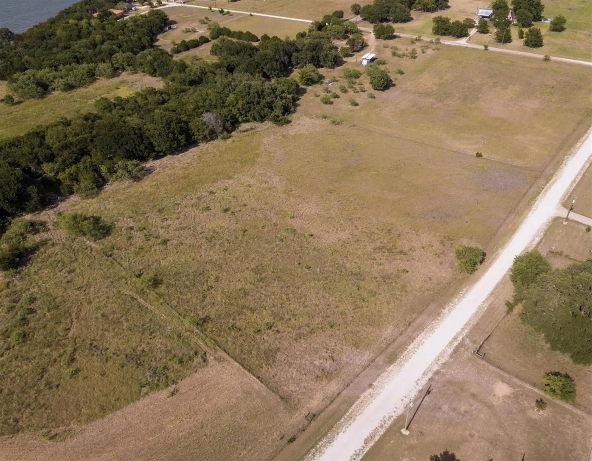 Expansive land parcel featuring a gravel road frontage, surrounding natural foliage, and open fields