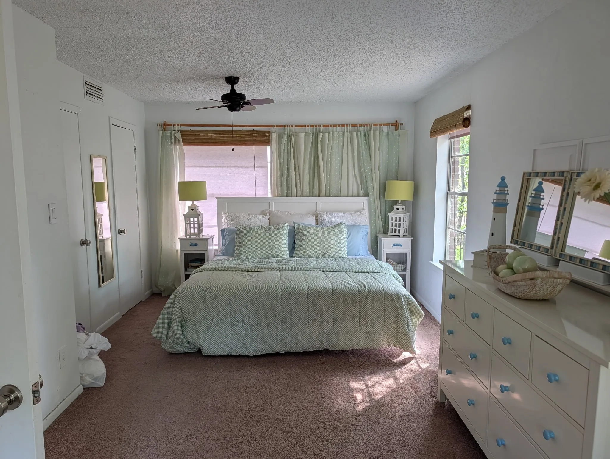 Carpeted primary downstairs bedroom with white walls and a ceiling fan