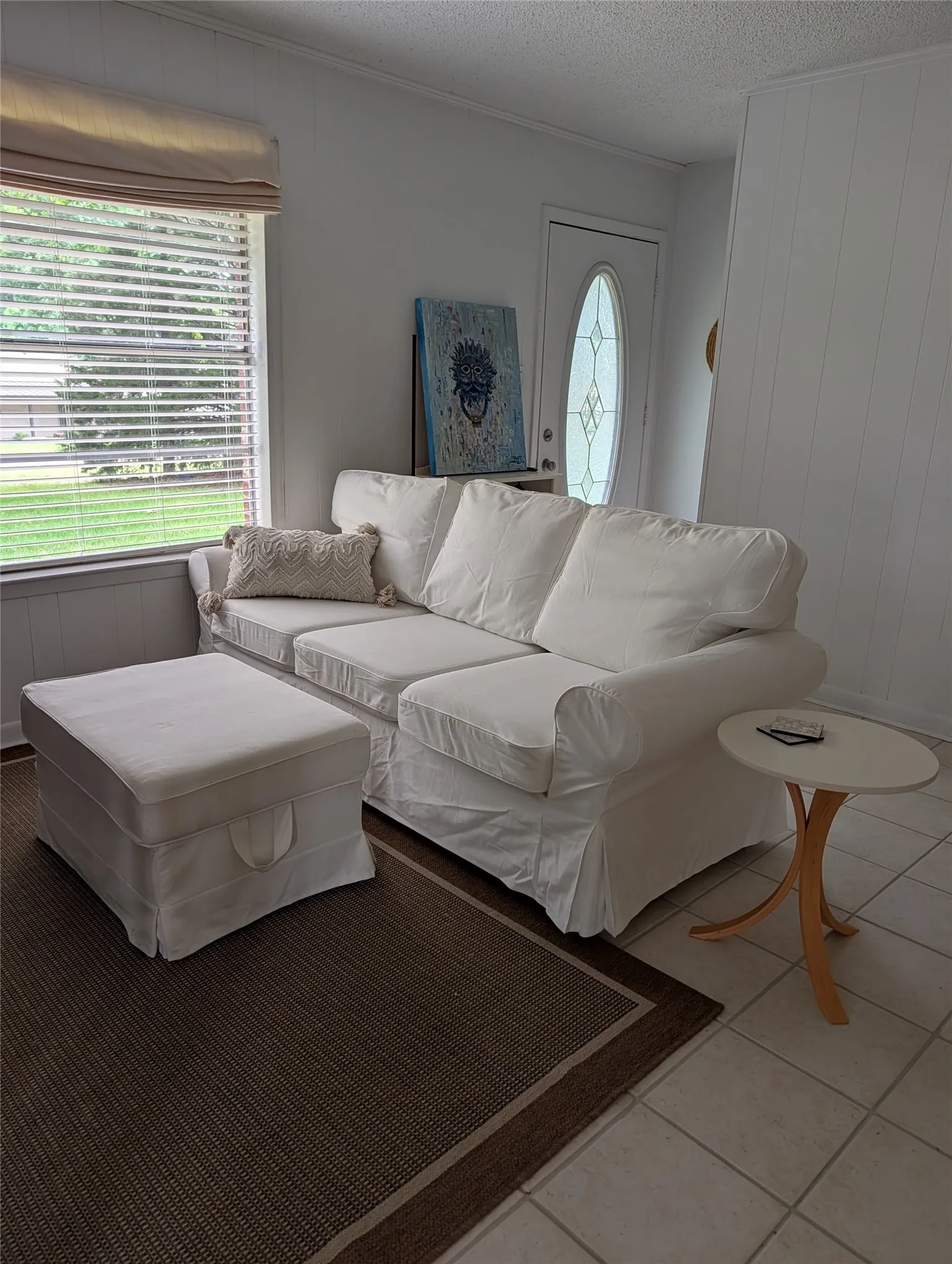 Living area featuring a single-pane window with horizontal blinds, a neutral roman shade, and a paneled accent wall