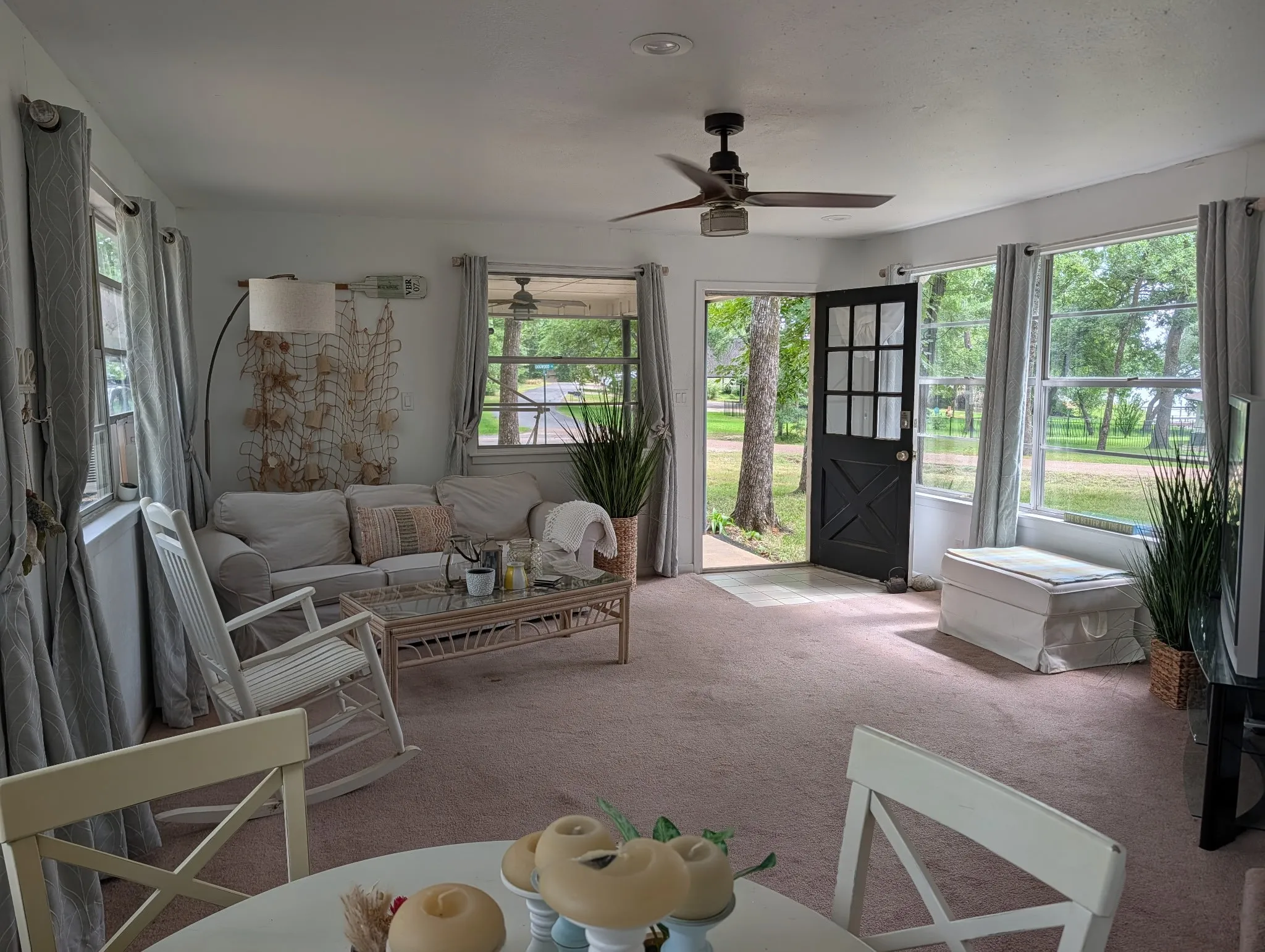 Living area featuring carpet flooring, multiple windows, a ceiling fan, and a black paneled door with glass inserts