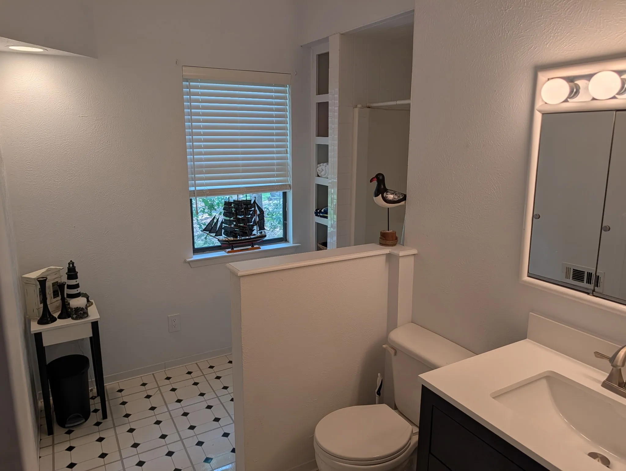 Upstairs bathroom featuring a black and white tiled floor, vanity with integrated sink, wall-mounted mirror with overhead lighting, and built-in shelving