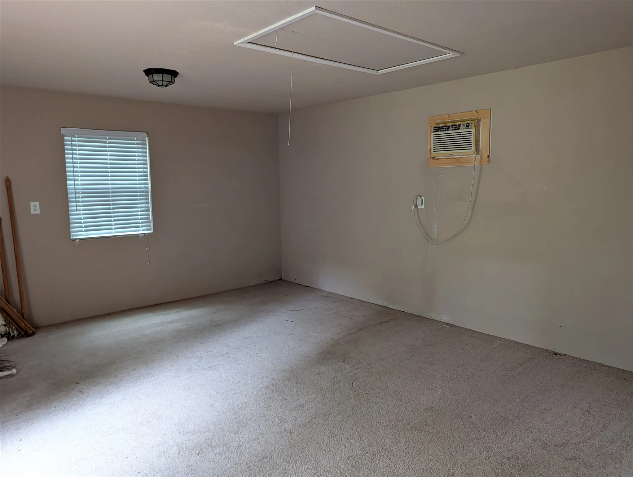 Carpeted interior Storage building with attic featuring a window with horizontal blinds, flush mount ceiling light fixture, and a wall-mounted air conditioning unit