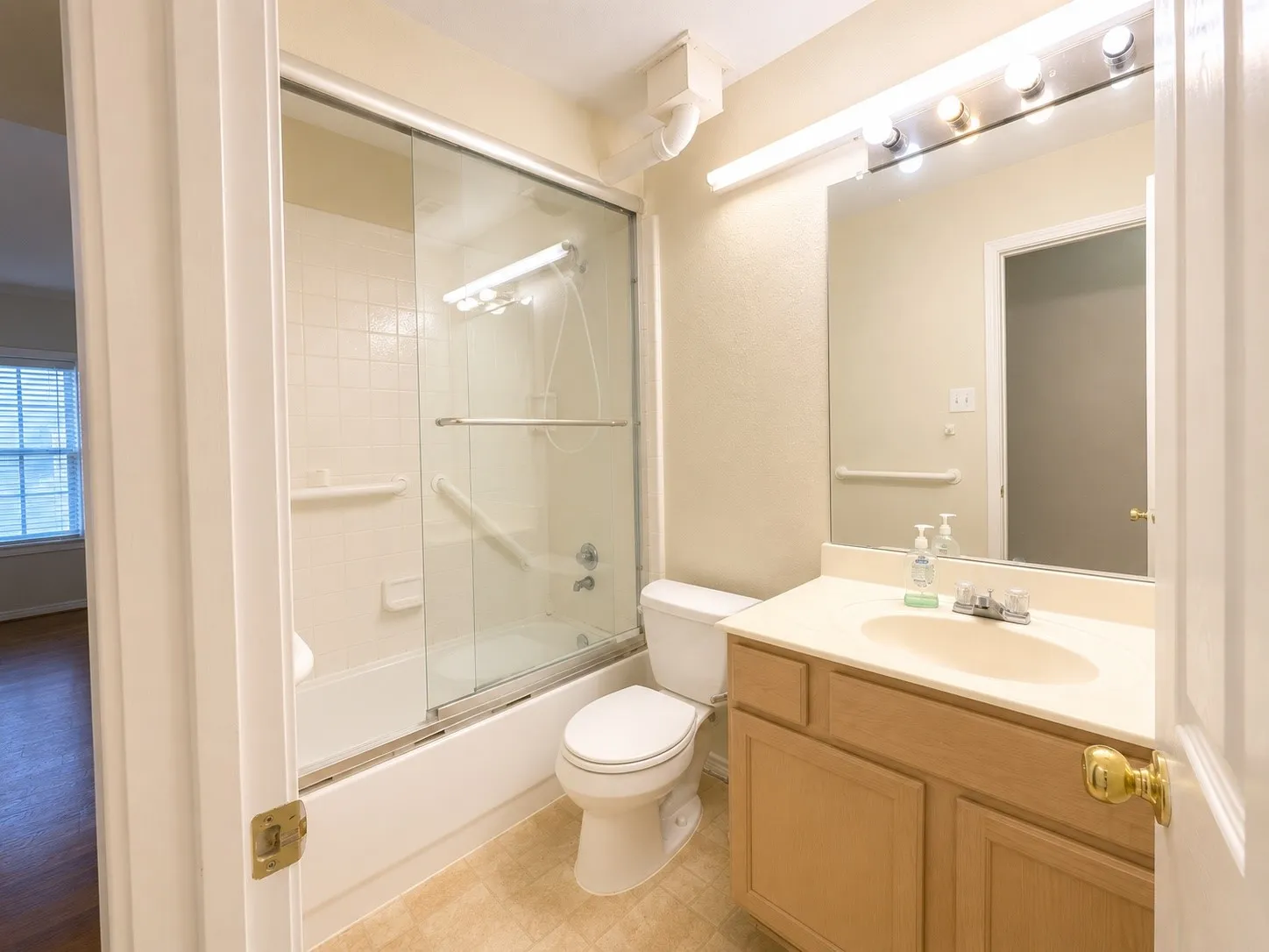 Bathroom featuring a light wood-finish vanity with a built-in sink, an overhead vanity light fixture, and a spacious mirror