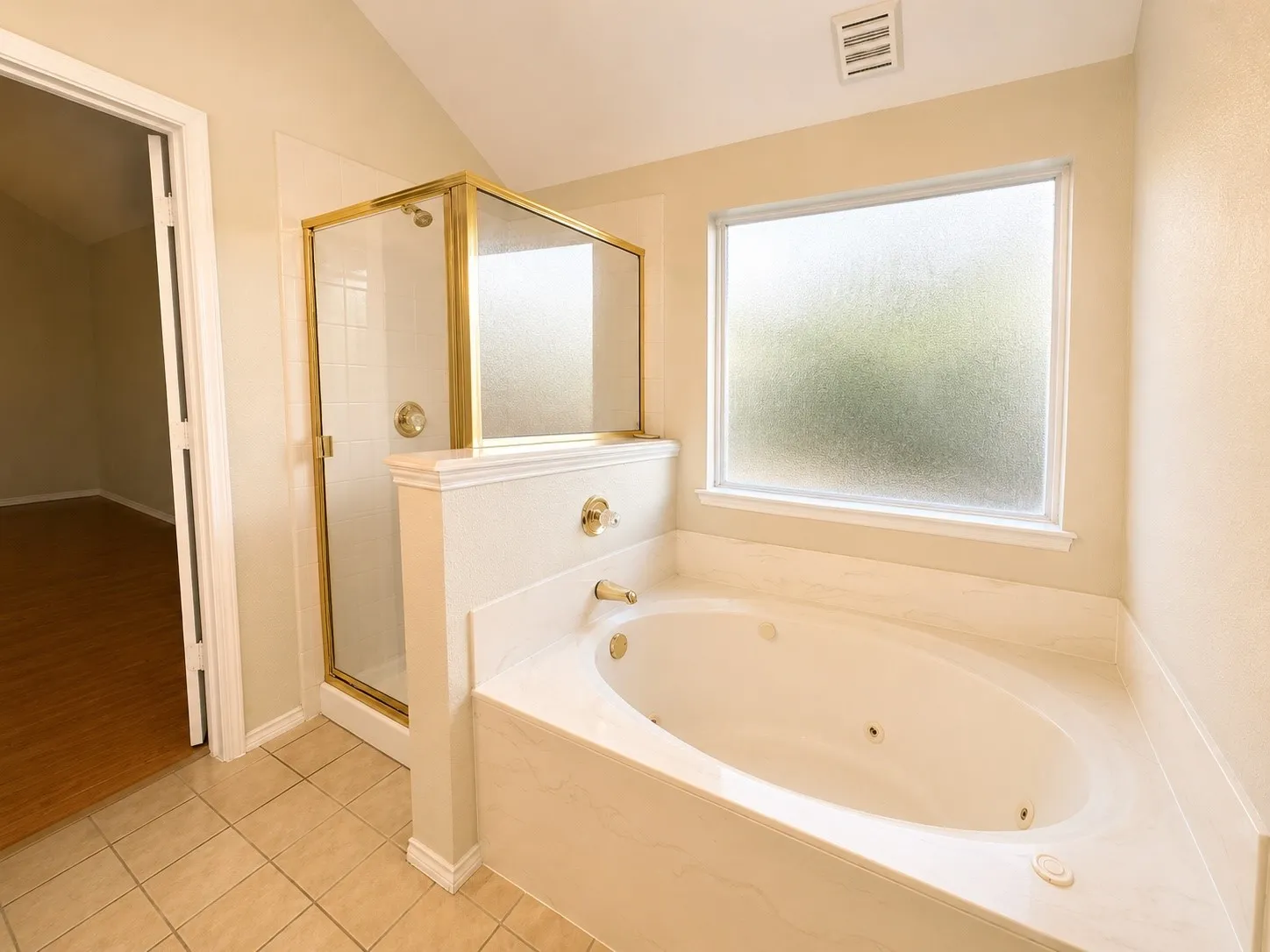 Soaking tub with integrated jets and gold-tone fixtures, complemented by a separate shower enclosure with gold-tone framing