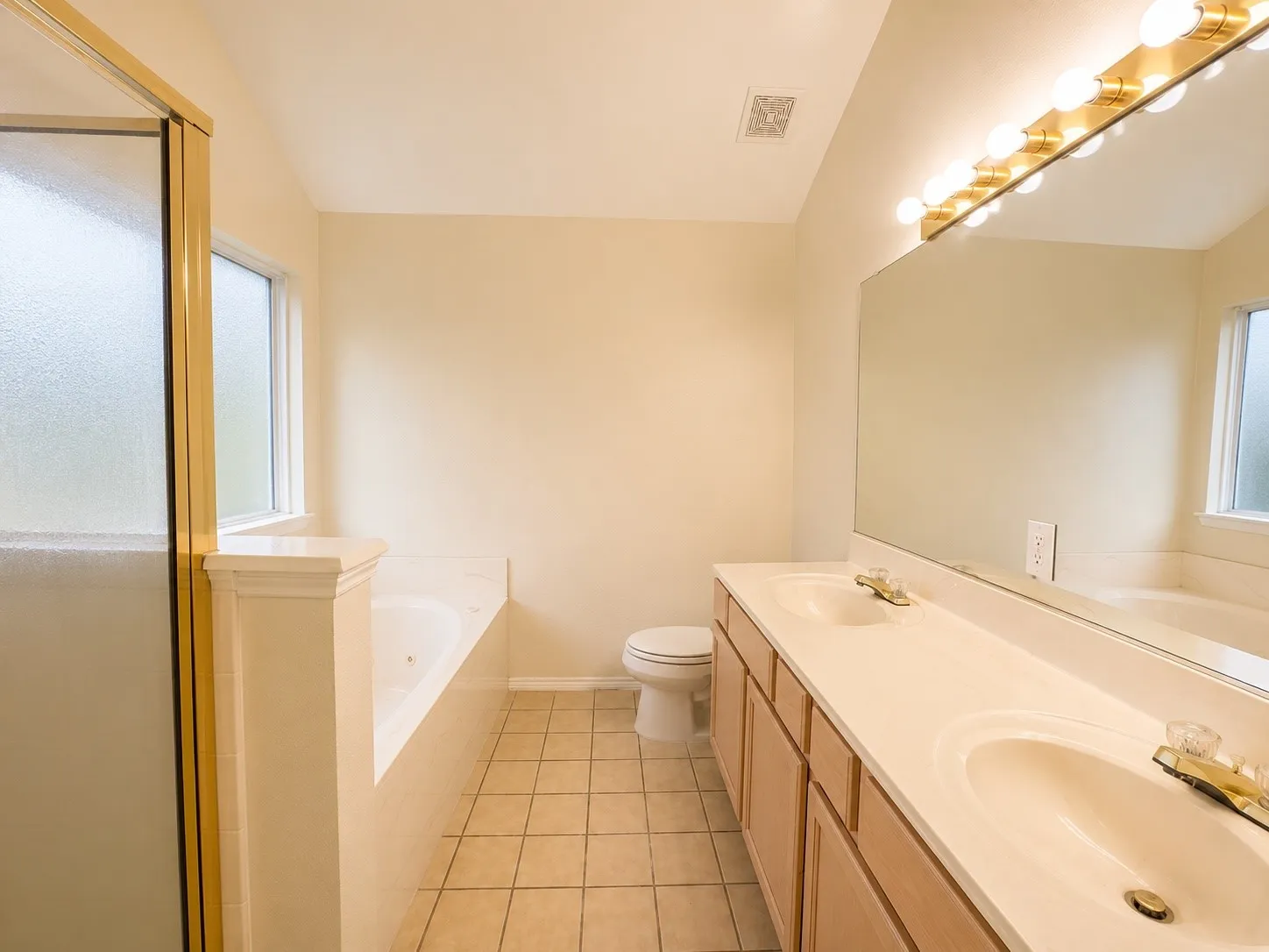 Bathroom featuring a dual vanity with integrated sinks, a built-in garden tub, a separate shower enclosure with a gold-toned frame, and ceramic tile flooring