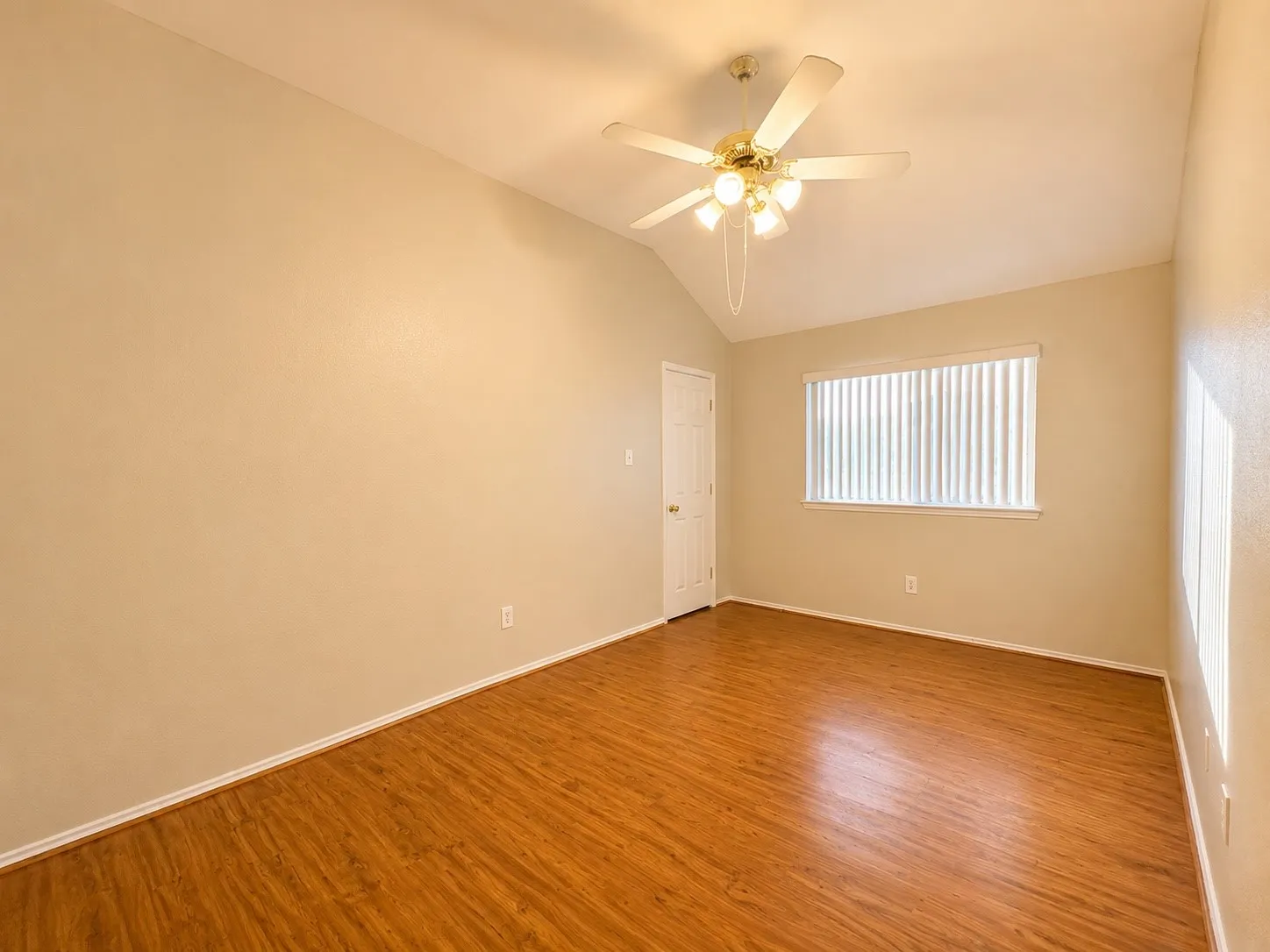 Vaulted ceiling room featuring wood-finish flooring, a ceiling fan with integrated lighting, and a window with horizontal blinds