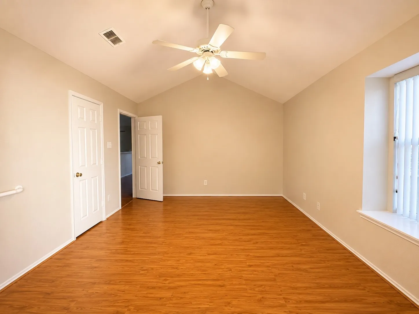Spacious room featuring vaulted ceilings, wood-finish flooring, a ceiling fan with integrated lighting, and vertical window blinds for controlled natural illumination