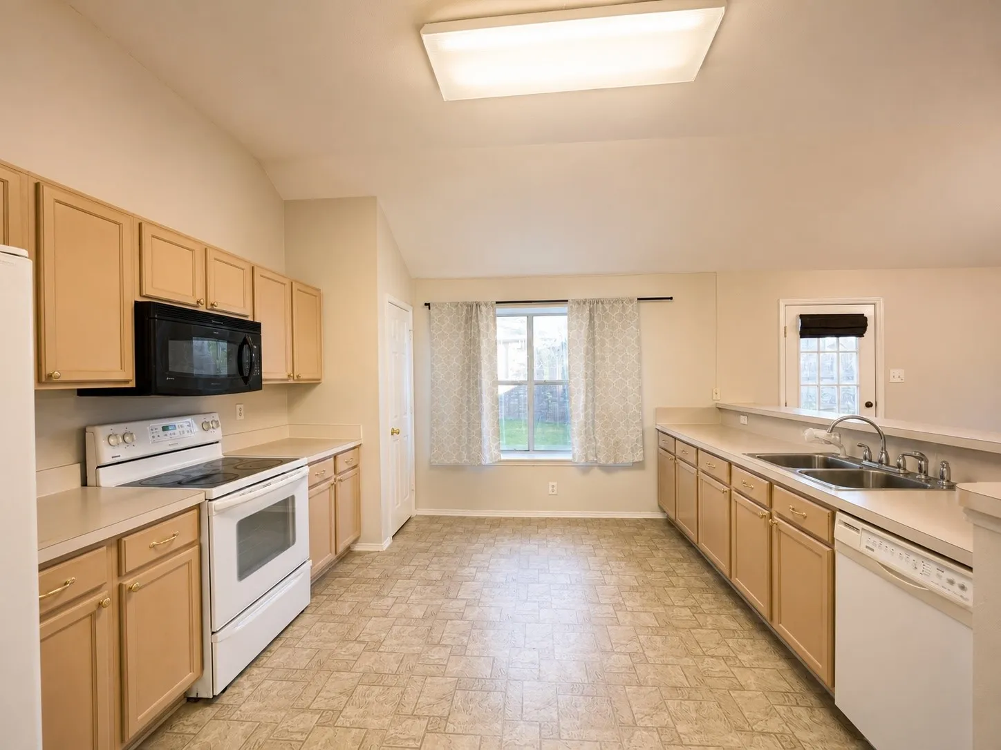 Kitchen featuring light wood-finish cabinetry, a double basin stainless steel sink, and a white electric range with an overhead microwave