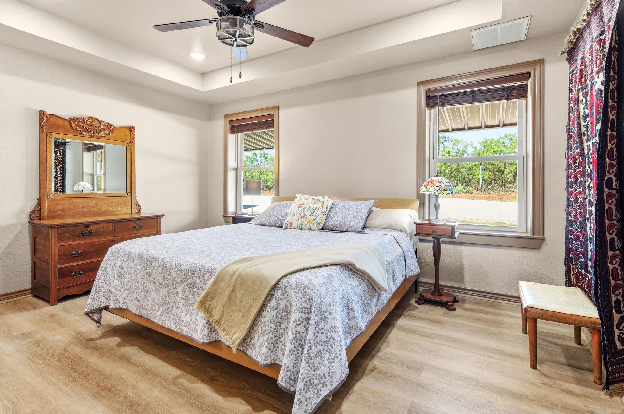Spacious primary retreat with tray ceilings and ceiling fan overhead, filled with natural light from windows- a relaxing, sunlit escape at the end of the day.