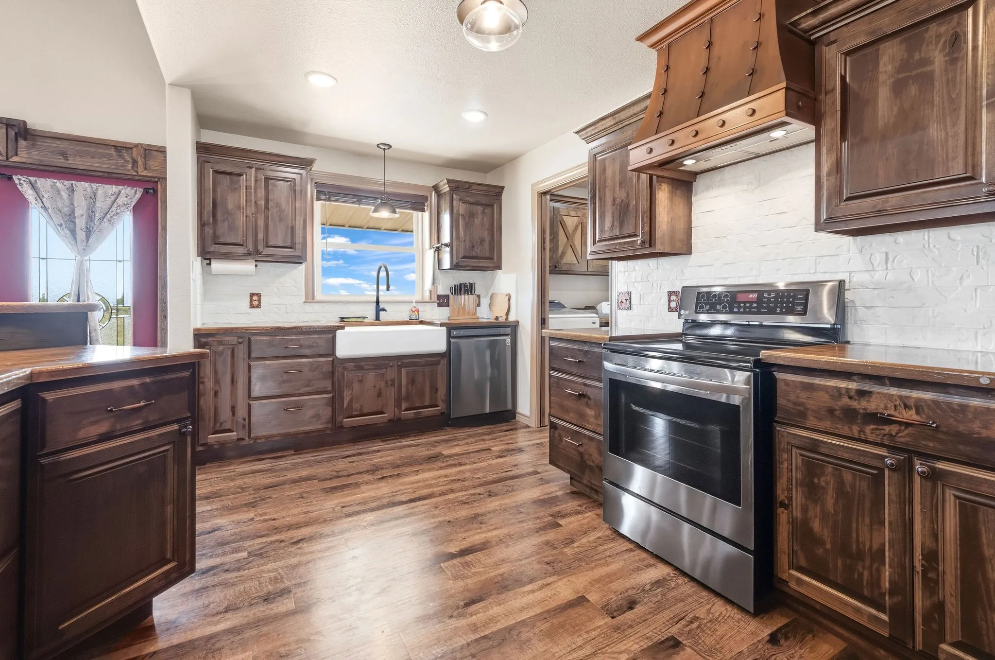 Country views fill the windows above a farmhouse sink, paired with stainless steel appliances and rich stained cabinetry for a kitchen that's as functional as it is full of character.