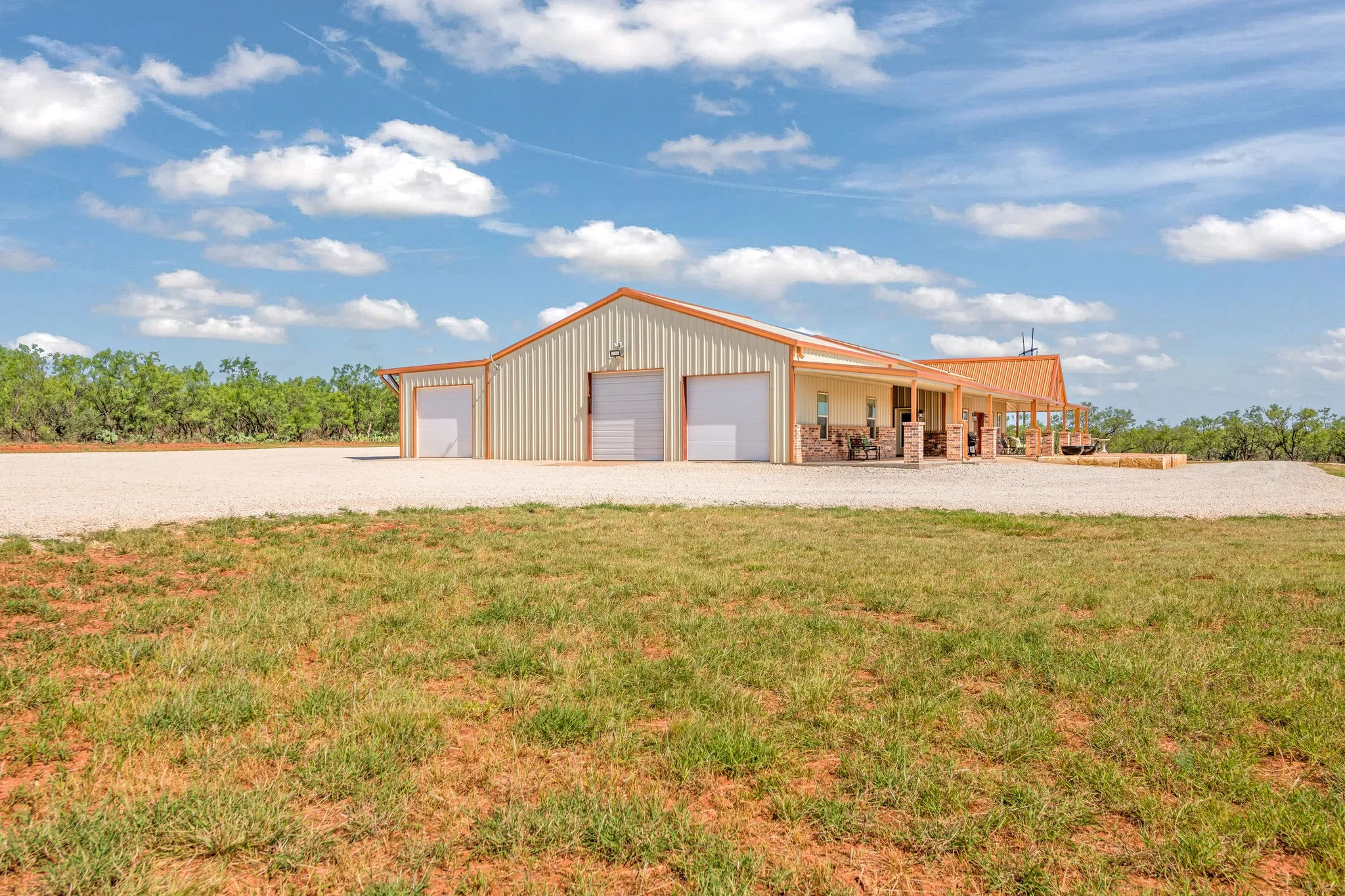 Side view of the shop shows off multiple large bay doors and a spacious concrete apron, connecting seamlessly to the covered breezeway and home beyond- a true multipurpose setup ready for vehicles, equipment or projects of about any size.