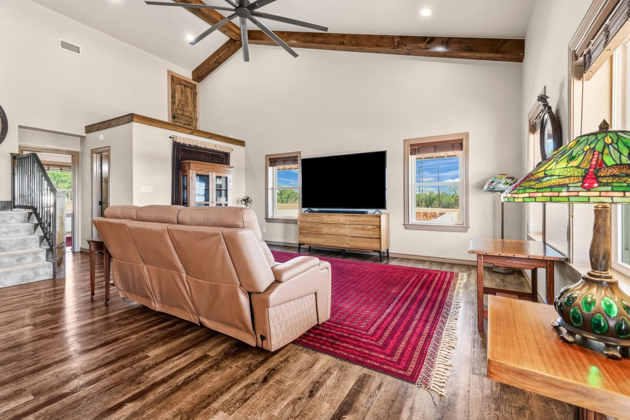 Vaulted ceilings with rustic wood beams and a statement fan soar over rich LVP floors, while big windows fill the space with natural light and country views-a warm welcoming spot to gather.