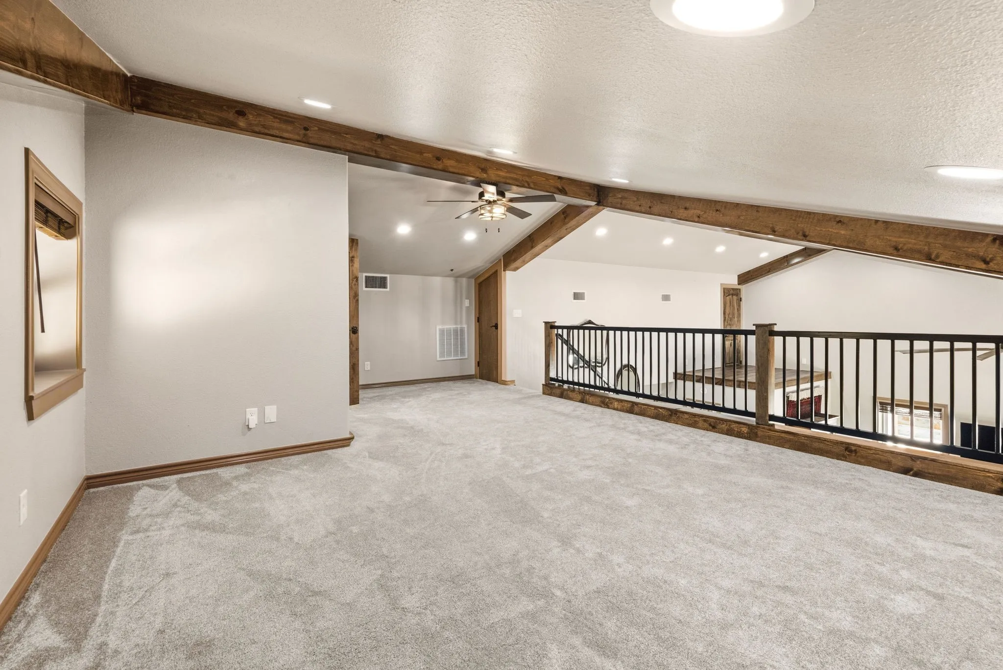 Another angle of the expansive loft, with metal railing overlooking the living space below and a door leading to the attic space that offers plenty of extra storage-endless possibilities for this bonus room.