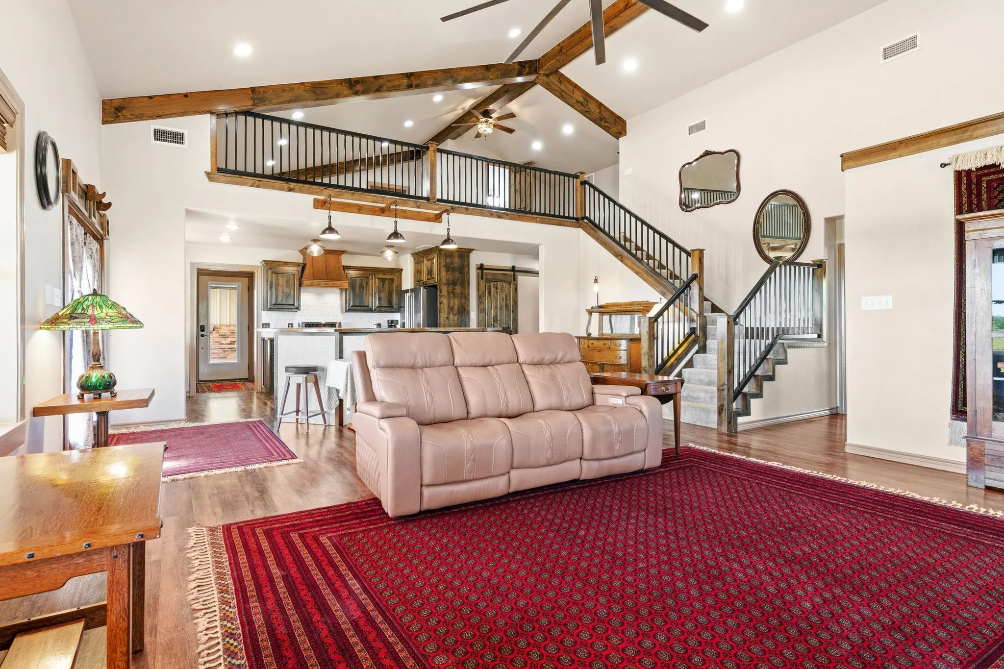 Open-concept living flows straight into the kitchen, with dramatic staircase and iron-railed loft overlooking it all beneath soaring beamed ceilings-a true showpiece for gathering and entertaining.