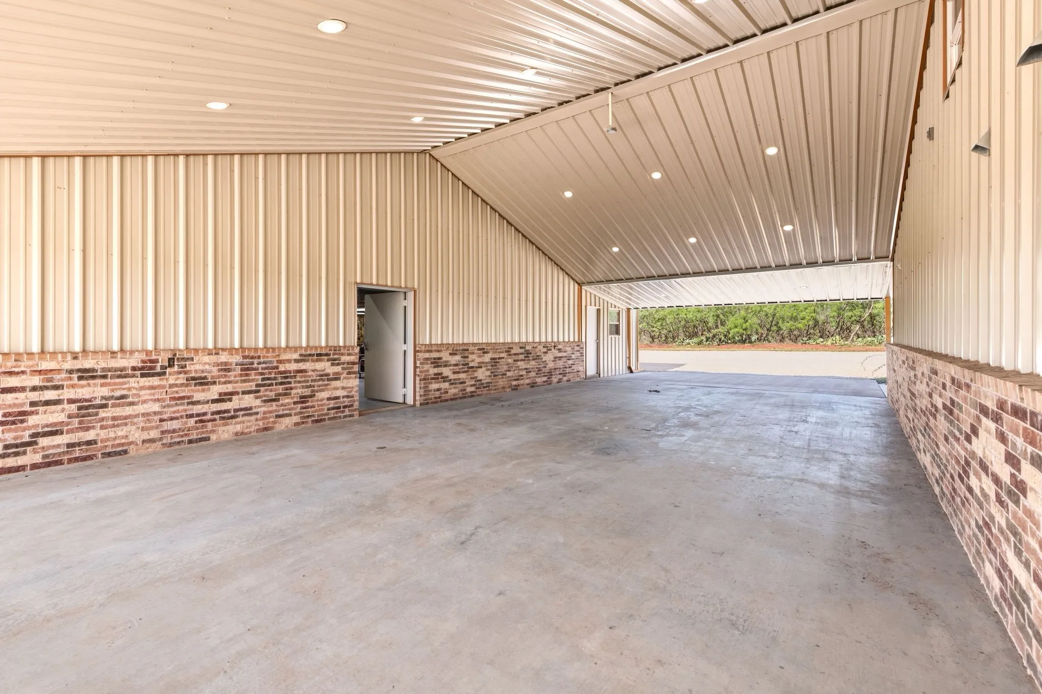 Expansive covered breezeway with spacious concrete pad, easily fitting four vehicles, connecting the home directly to the shop for easy, weather-protected access year-round.