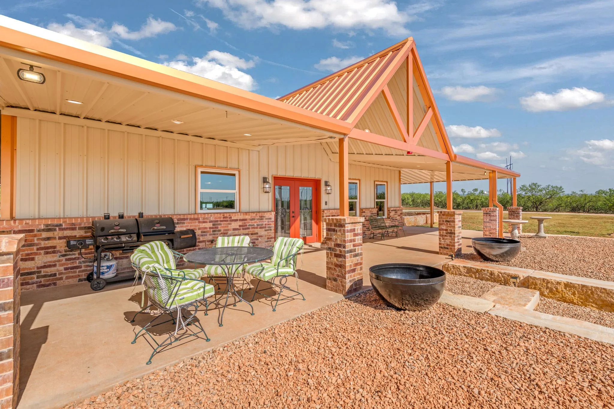 Covered front porch with soaring metal roofline and exposed beams., brick columns nicely landscaped with large limestone blocks and beautiful metal pots to fill with your choice of plants or leave empty.