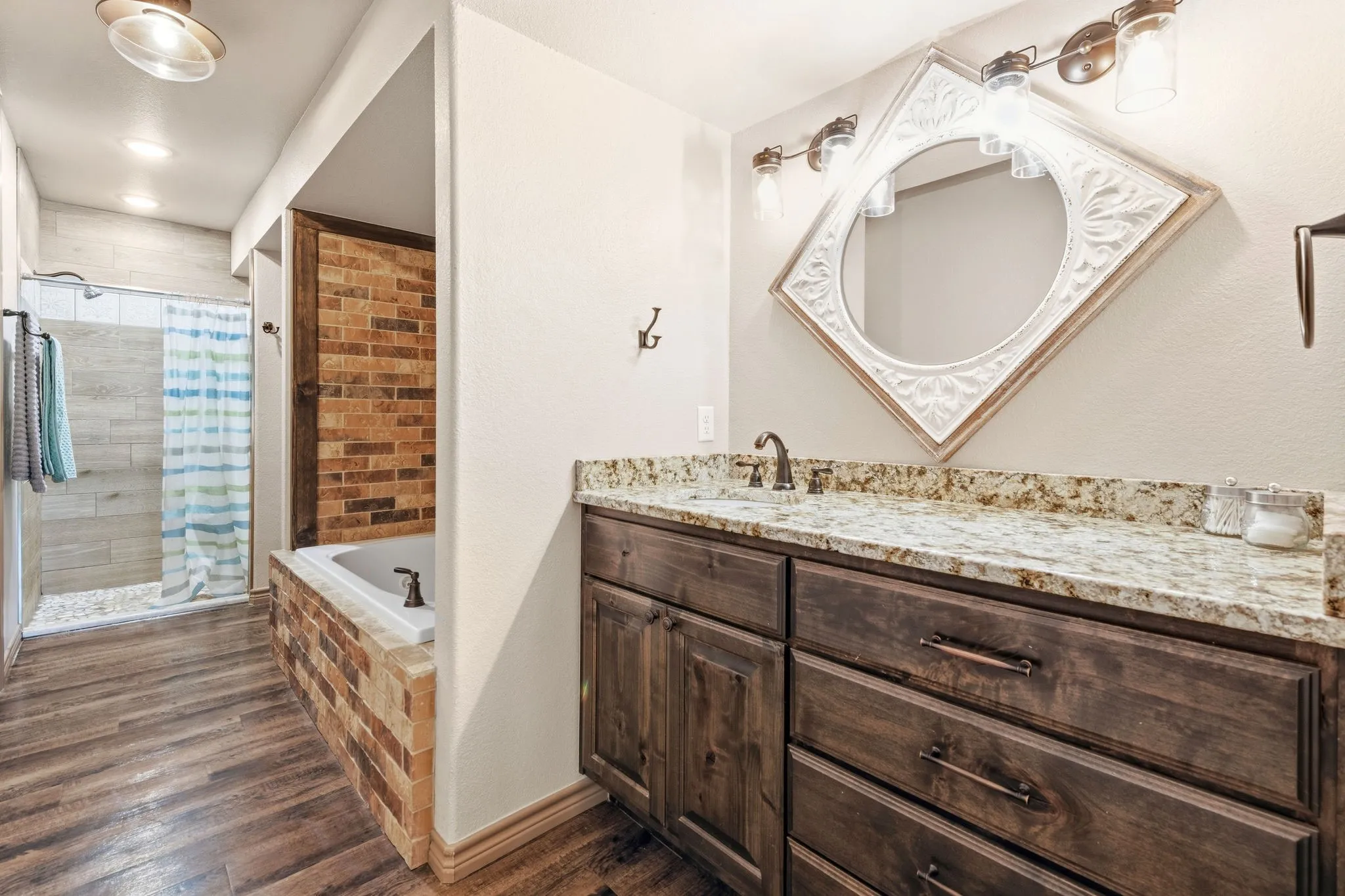 Spa-like en-suite with granite countertop and rich stained cabinetry, a brick accented jacuzzi tub for soaking away the day, plus a separate standing shower for easy everyday convenience.