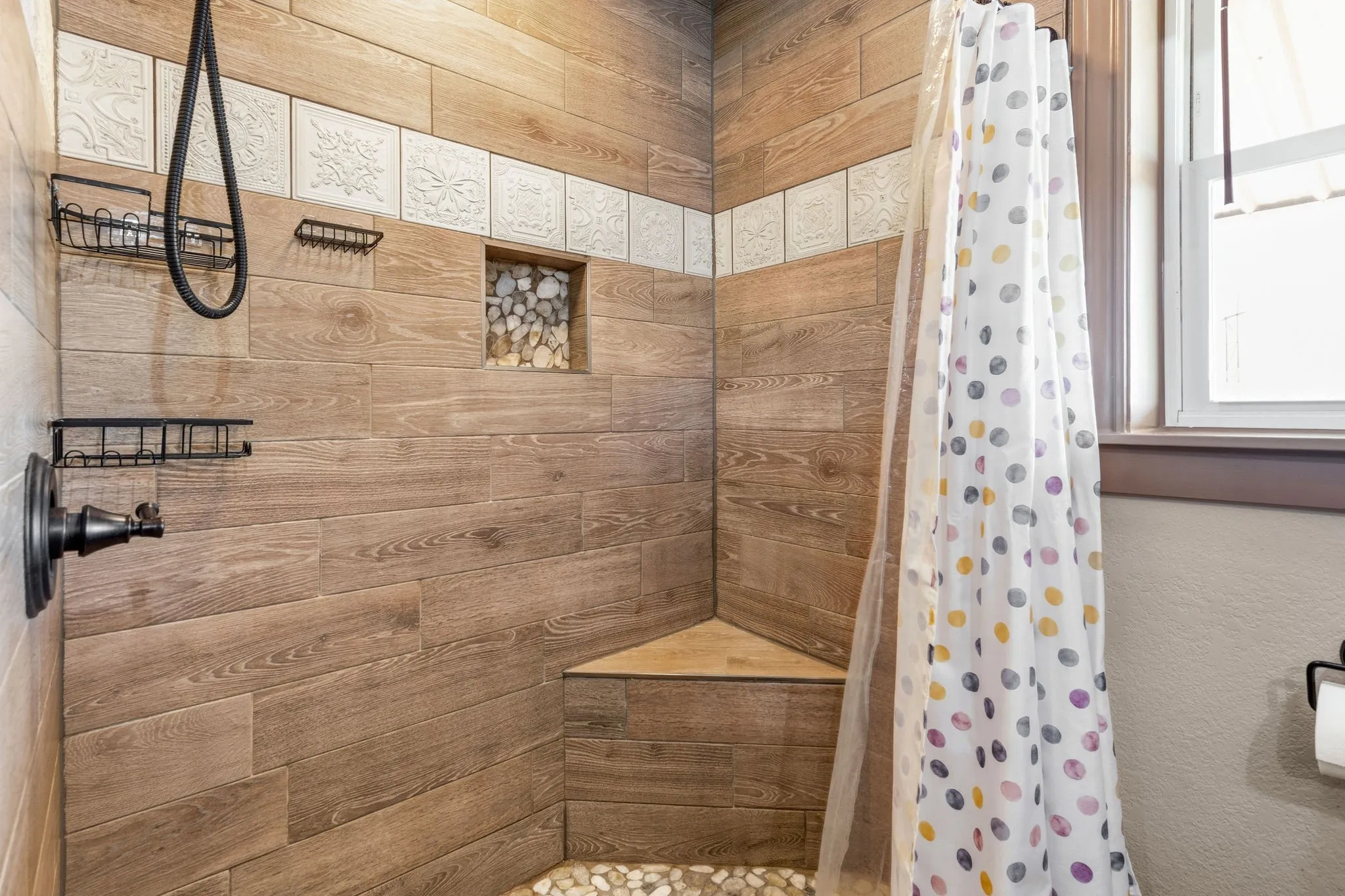 Wood-look title creates a warm, earthy backdrop in this standing shower, complete with built-in corner bench and river rock accent for a spa-like touch.