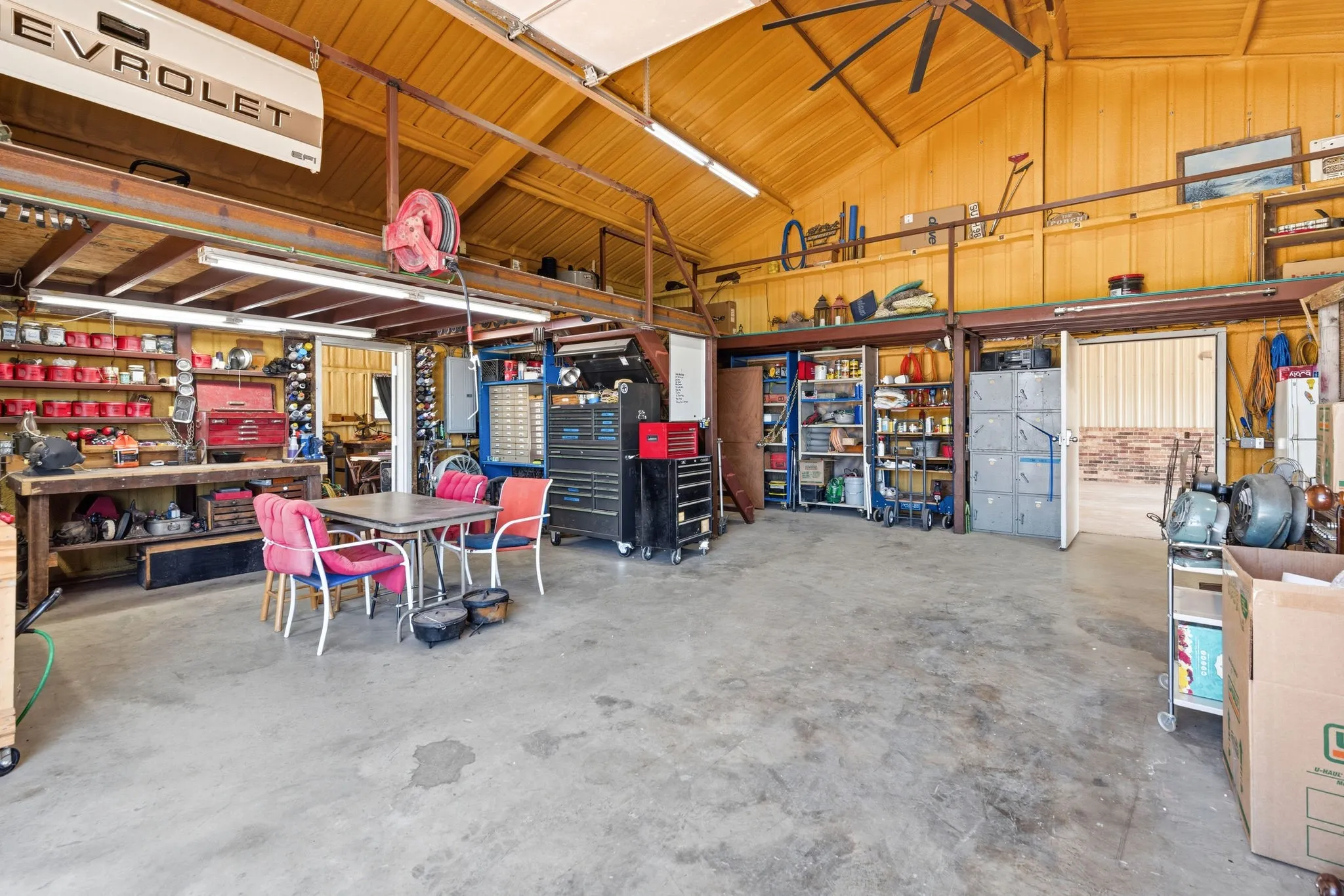 Another view of this expansive shop, showcasing towering ceilings with built-in shelving and workbenches, plus electricity and plumbing already in place- ready to handle whatever project you bring to it.