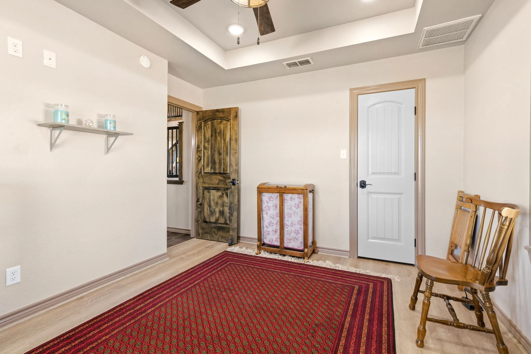 Bright secondary bedroom with tray ceiling and ceiling fan, tucked-in shelving for extra storage, and a deep walk in closet with built-in shelving and hanging rods behind the white door.