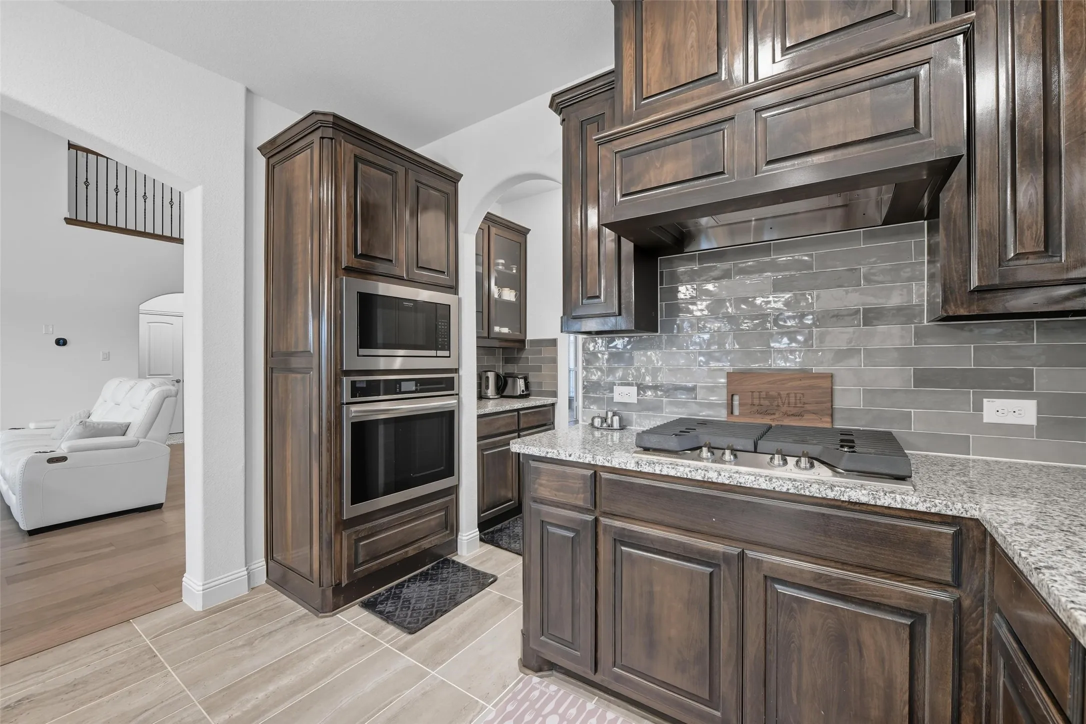 Kitchen featuring rich wood cabinetry, built-in stainless steel microwave and oven, a gas cooktop, granite countertops, and a gray subway tile backsplash