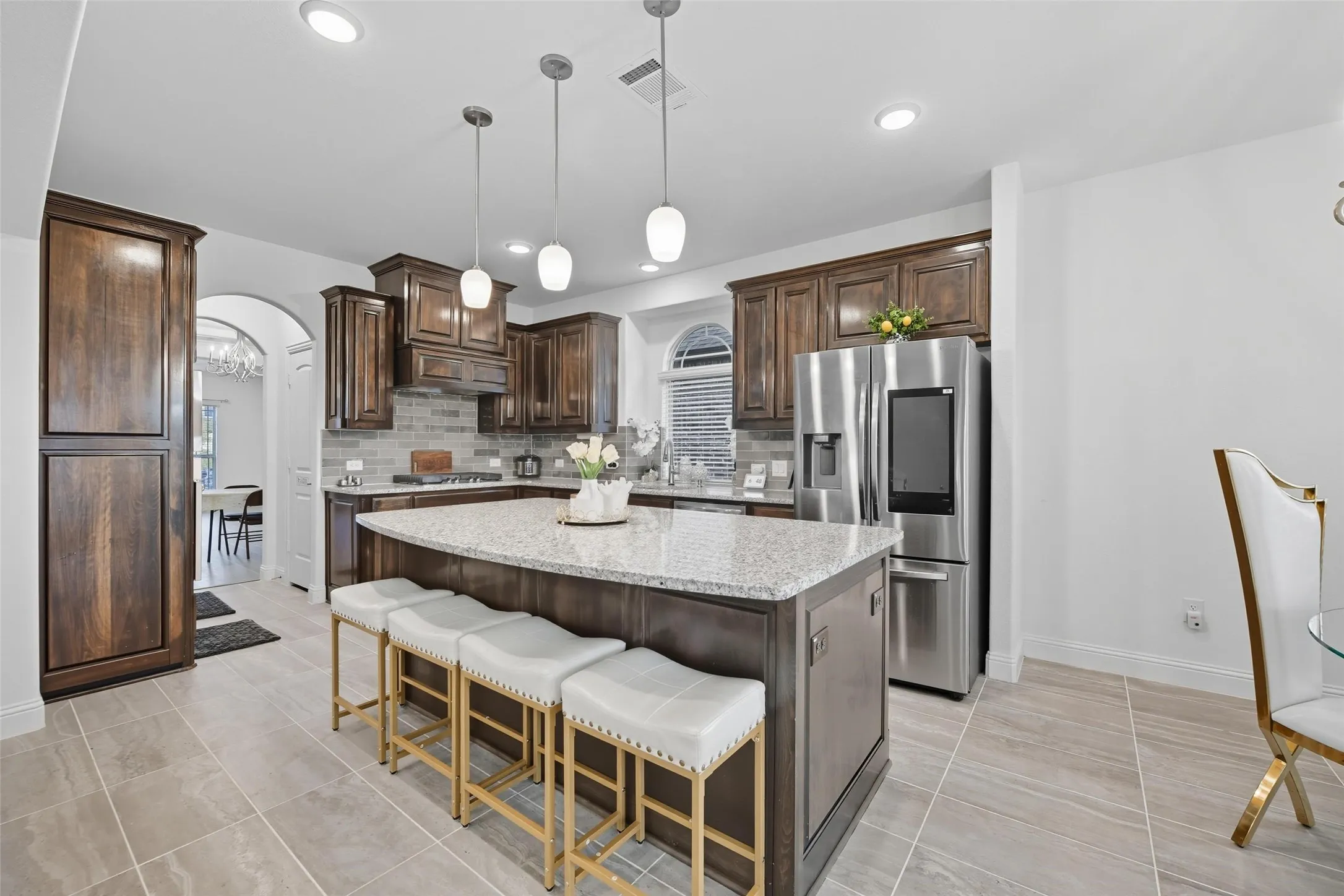 Kitchen featuring a large island with a light-toned countertop, stainless steel refrigerator, dark wood cabinetry, and a tile backsplash