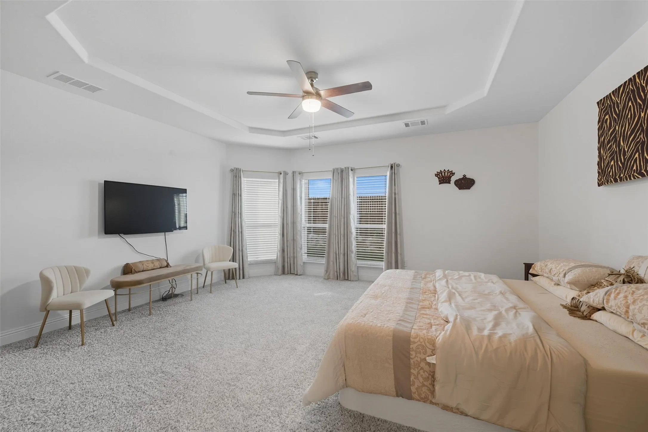 Spacious room featuring a tray ceiling with a ceiling fan, light-toned carpeting, and a bay window configuration with blinds and drapes