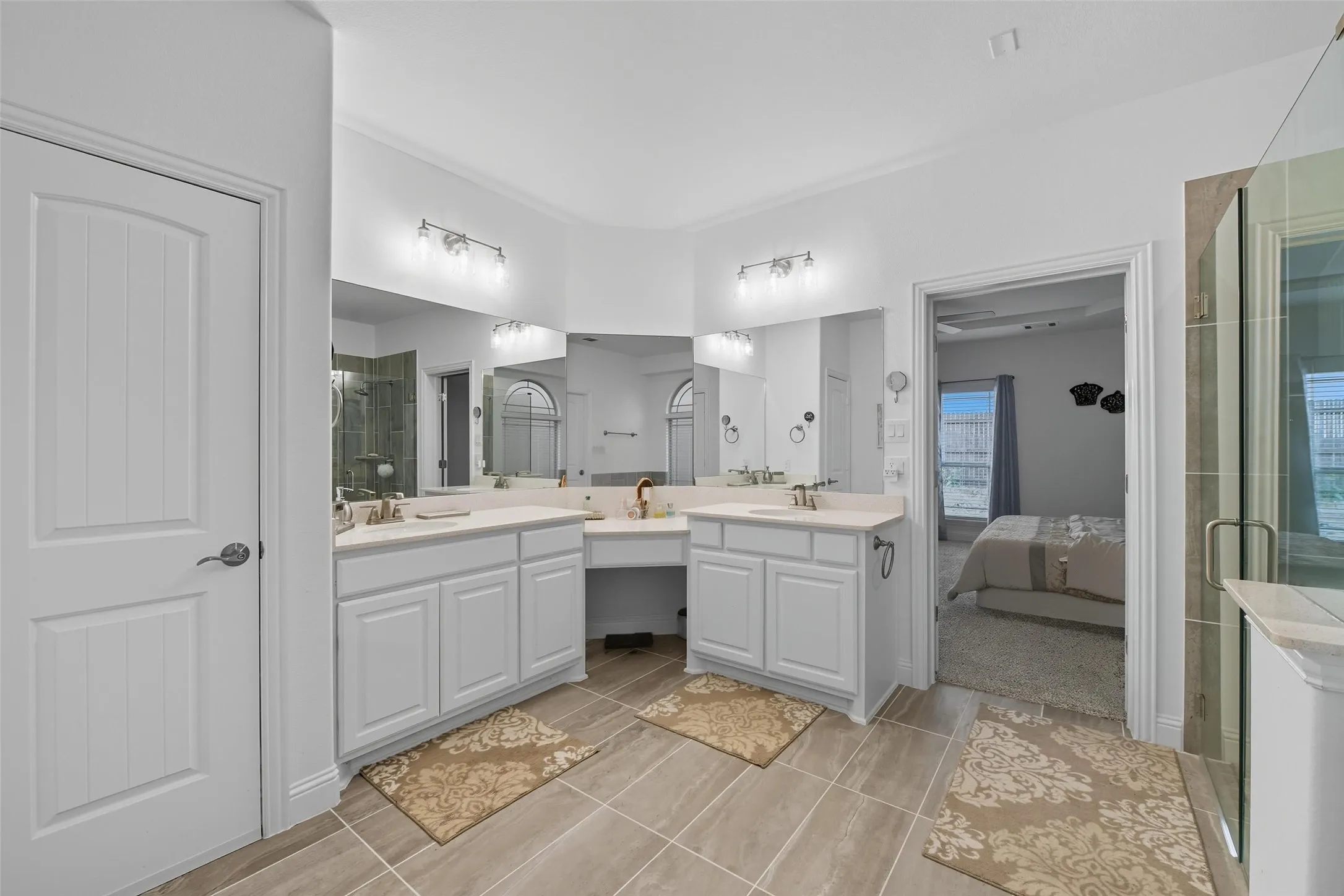 Bathroom featuring dual vanities with white cabinetry and light-toned countertops, a glass-enclosed shower, large wall mirrors, and tiled flooring