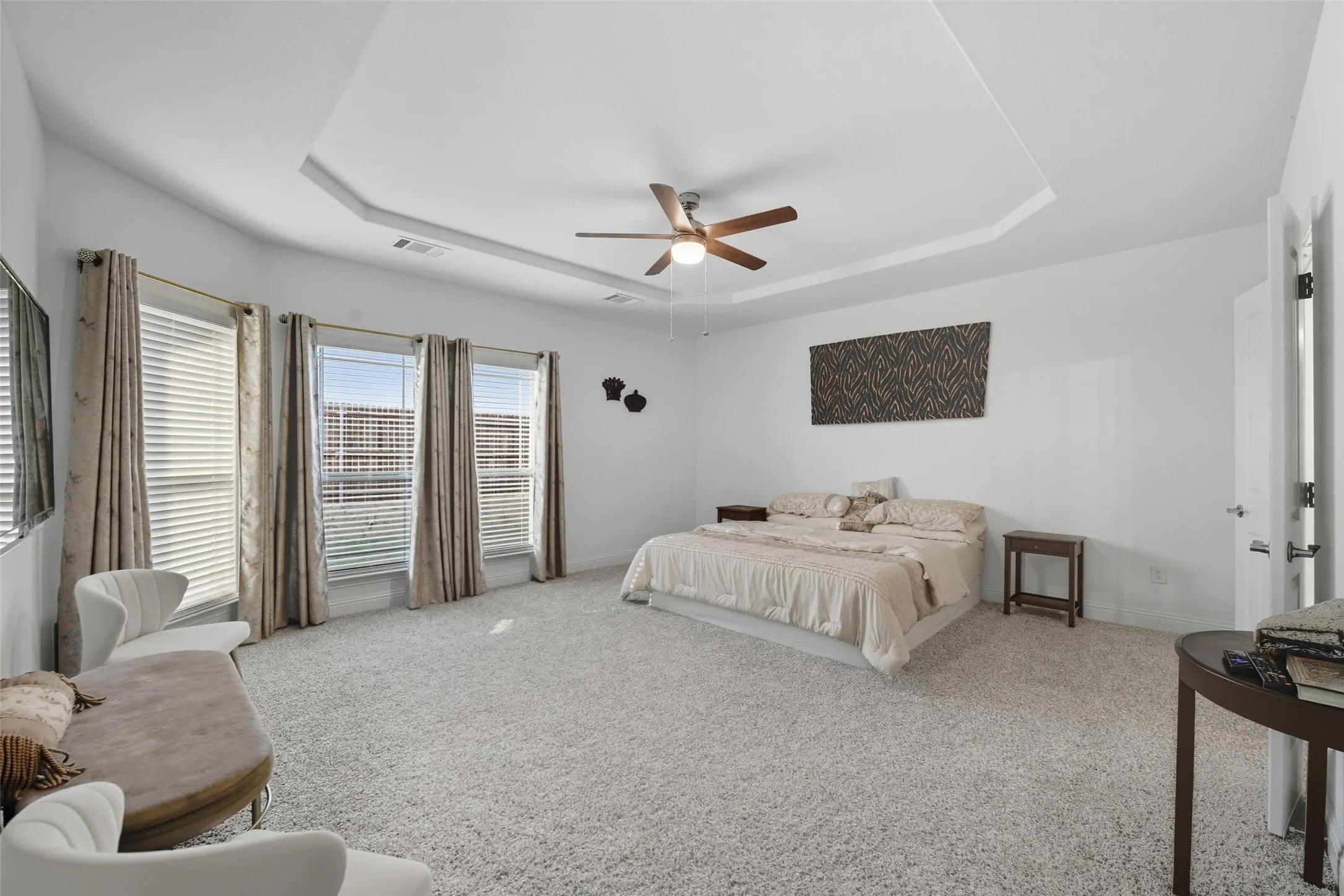 Spacious room featuring a tray ceiling, ceiling fan, and light-toned carpet