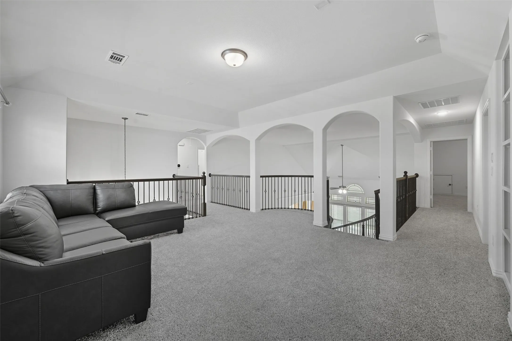 Spacious loft area featuring light gray carpeting, white walls, and decorative arched openings