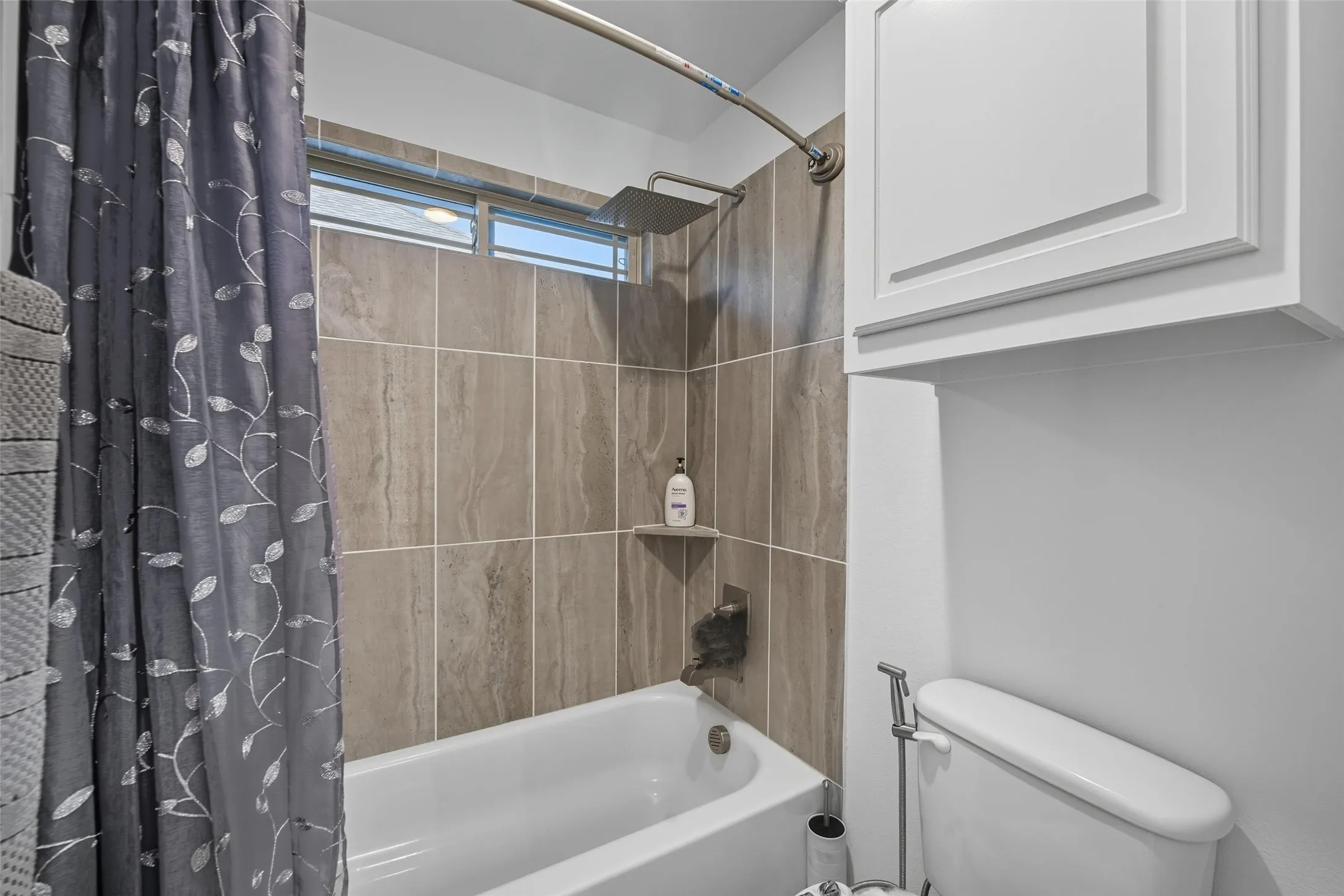 Bathtub with floor-to-ceiling tile surround, built-in shelf, rainfall showerhead, and transom window