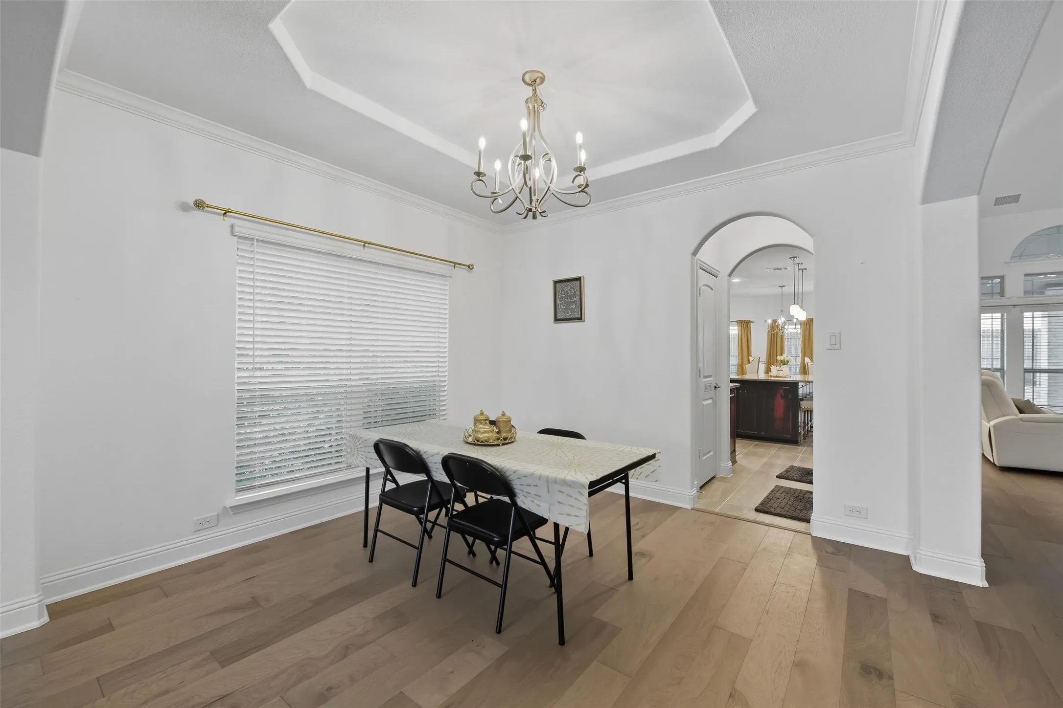 Dining area featuring wood-finish flooring, a tray ceiling with a chandelier, and an arched doorway