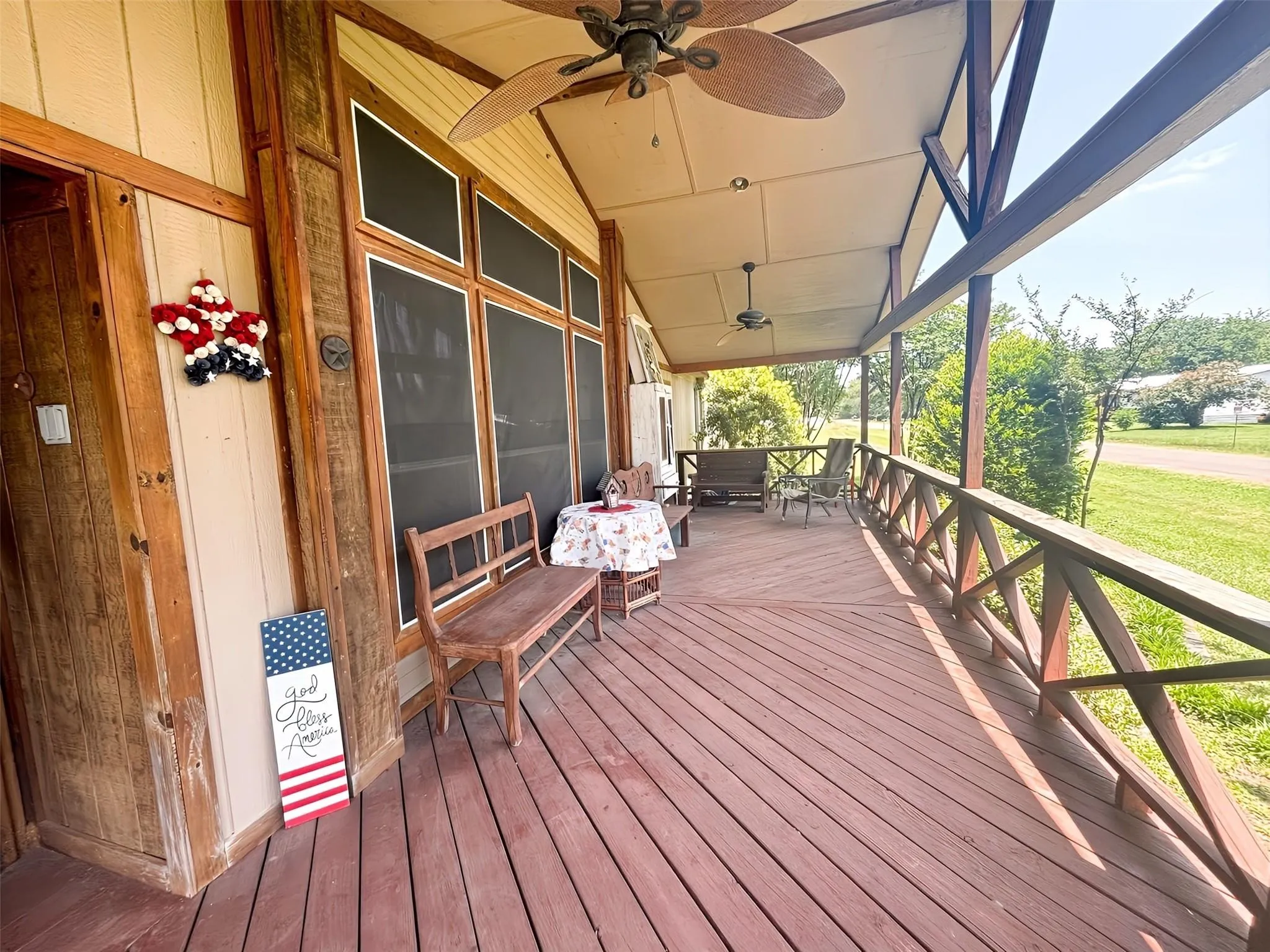 Expansive covered porch featuring wood-finish flooring, exposed structural beams, ceiling fans, and a decorative wood railing