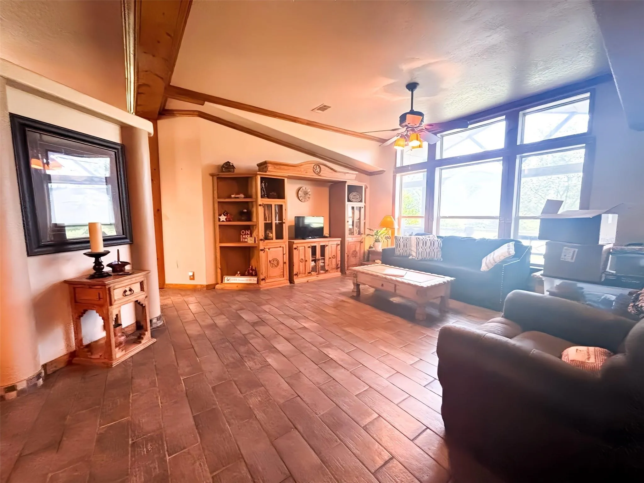 Spacious living area featuring wood-finish tile flooring, vaulted ceilings with exposed wood beams, and a built-in entertainment center