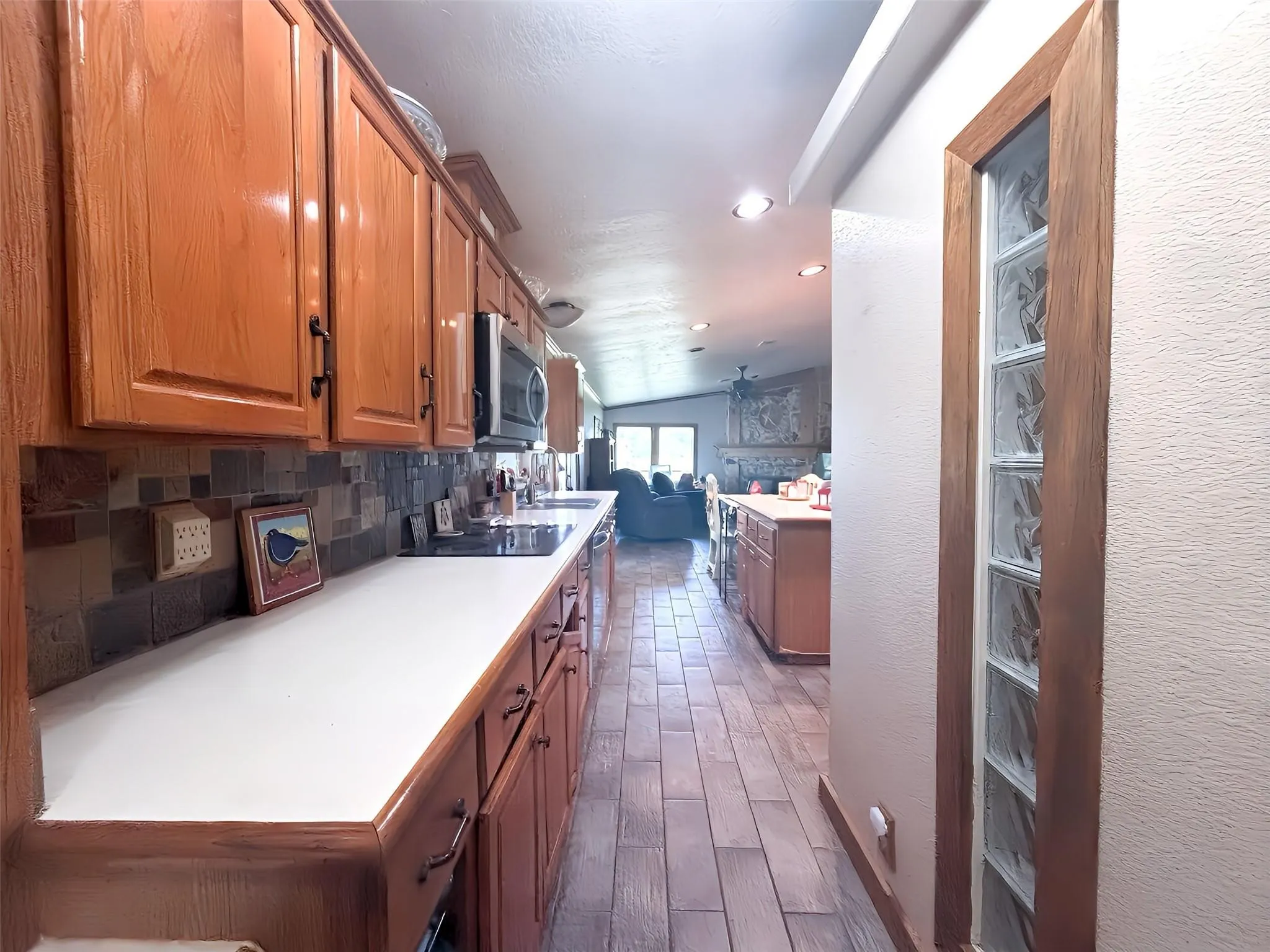 Galley kitchen featuring wood cabinetry, white countertops, tile backsplash, built-in microwave, and recessed lighting